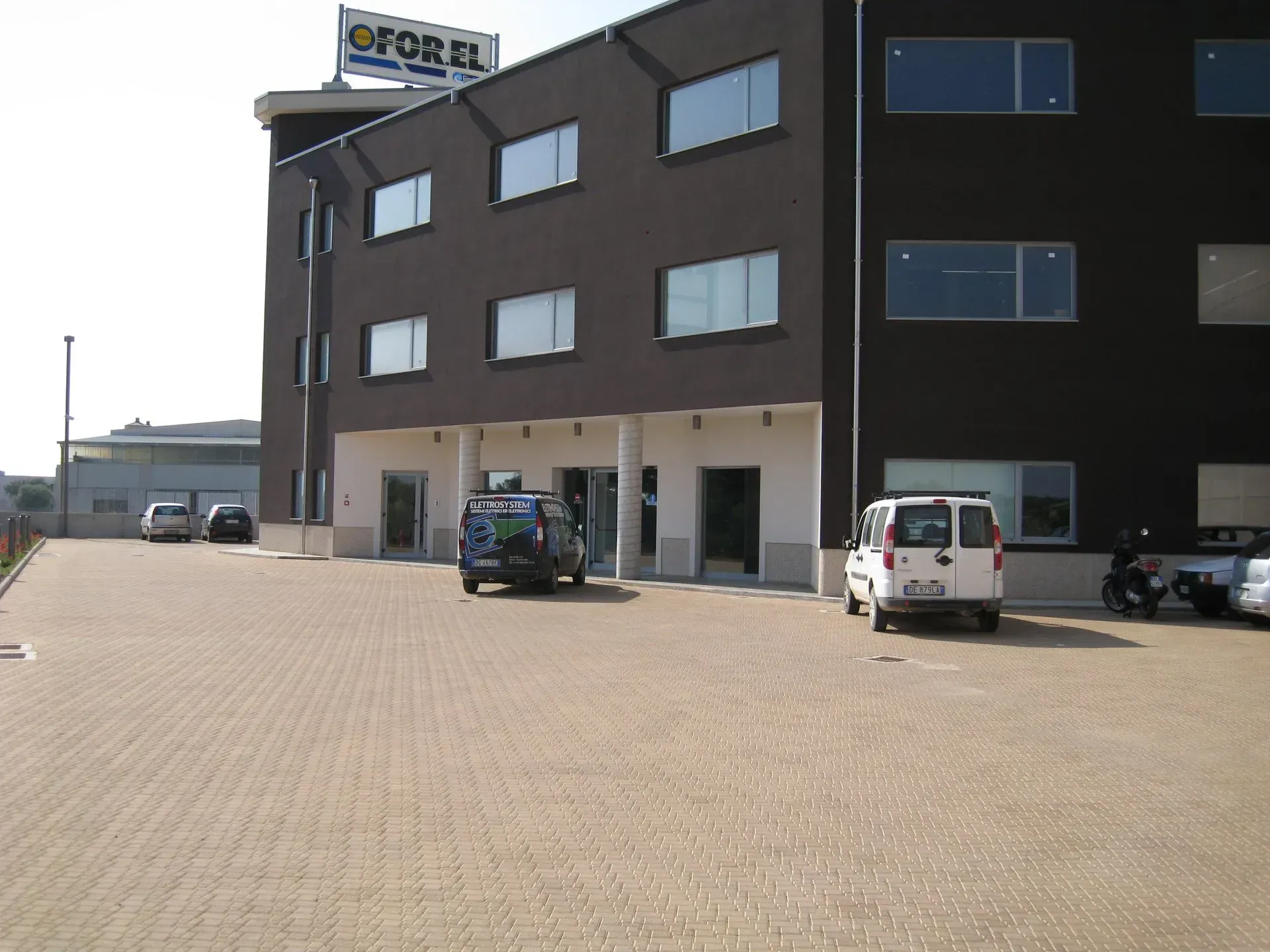 Edificio marrone scuro con parcheggio e auto. Cartello 