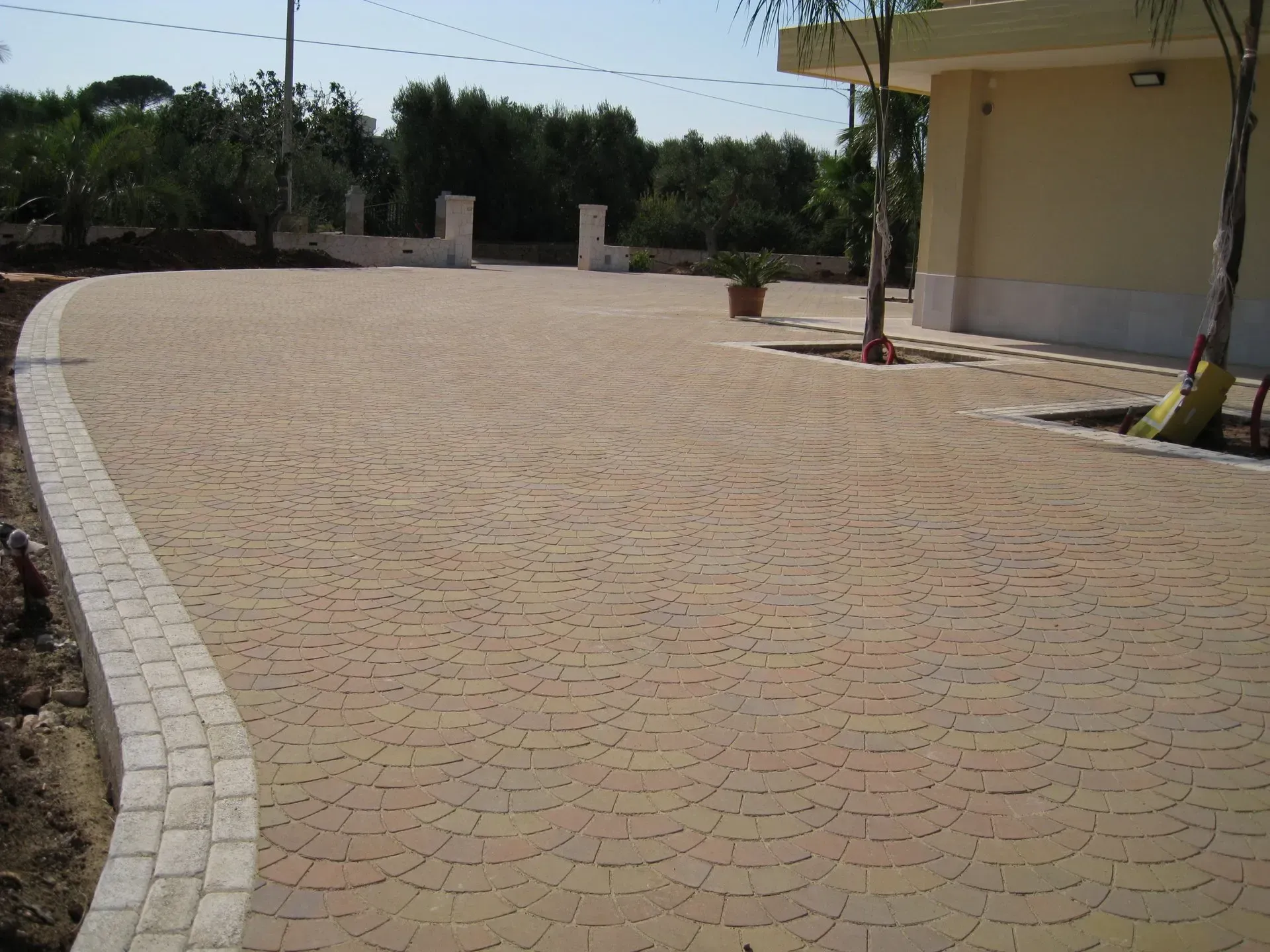Vialetto pavimentato con piastrelle beige a motivi geometrici, delimitato da blocchi di colore chiaro, che conduce a un edificio.