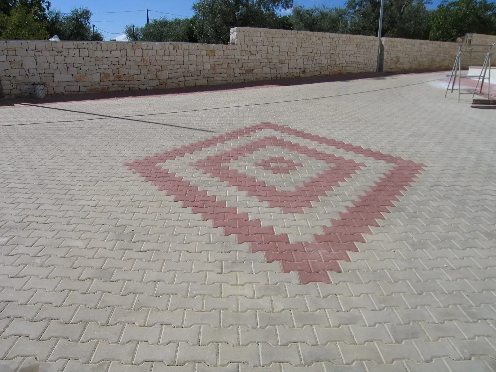 Area pavimentata con motivo a rombi rossi e beige. Basso muro di pietra sullo sfondo.