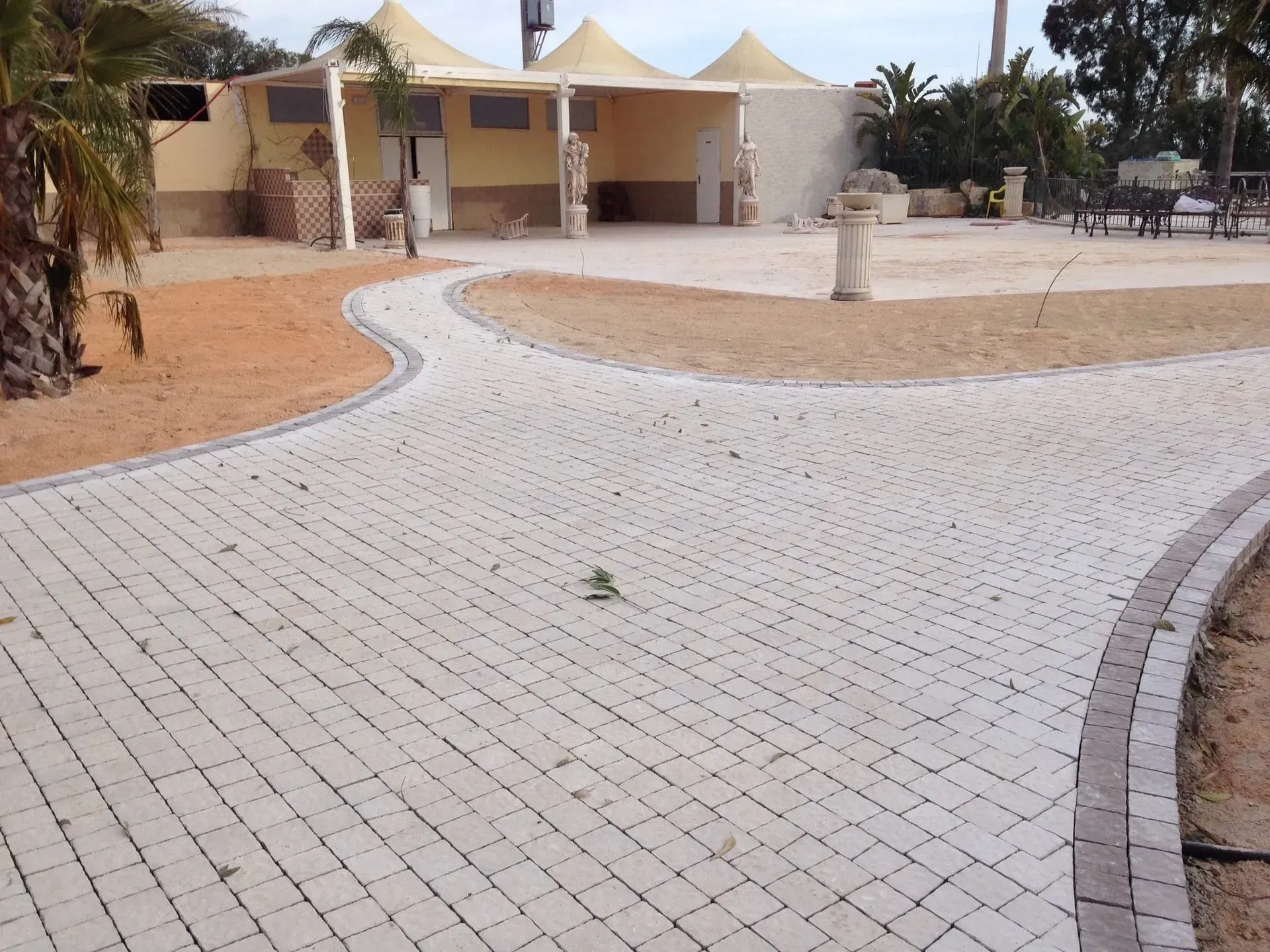 Sentiero lastricato che si divide in due e conduce a un edificio beige con una tettoia. Ambiente desertico.