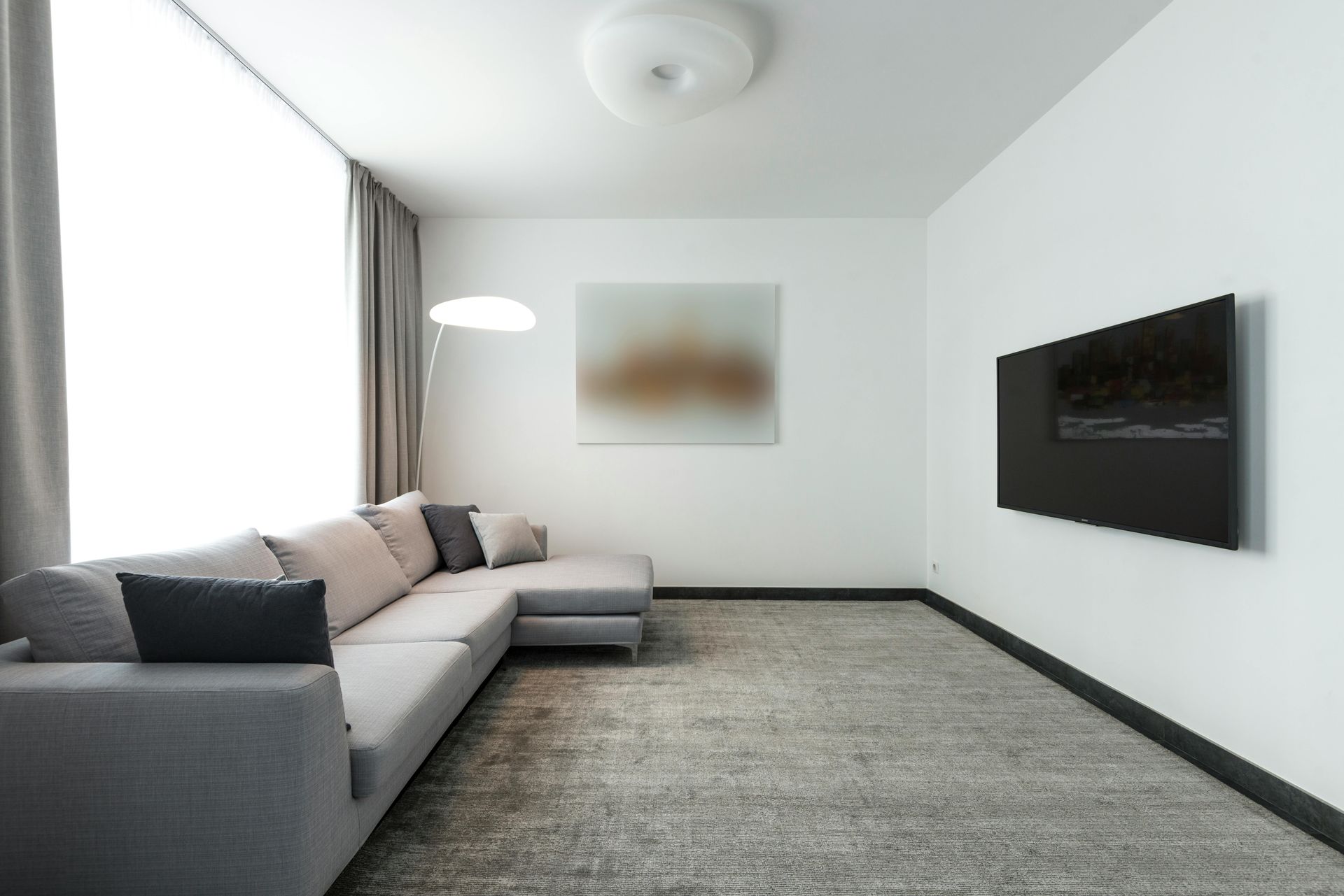 Modern living room with gray sectional, large TV on wall, and neutral-toned artwork.