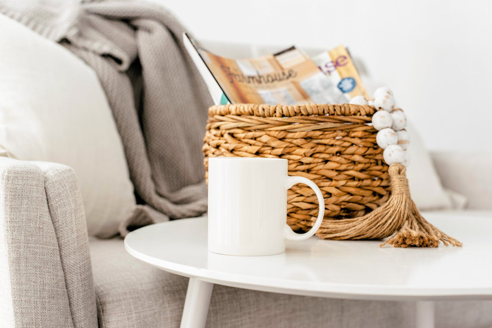 White mug on a round table, next to a wicker basket with magazines and decorative beads.