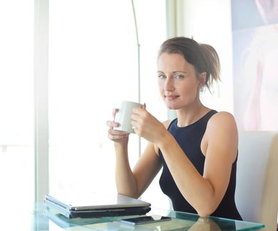 A woman is sitting at a desk drinking a cup of coffee