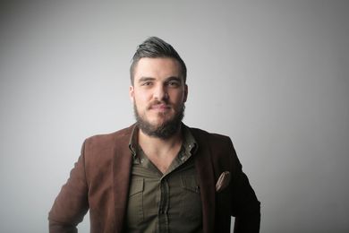 A man with a beard is wearing a brown jacket and a green shirt.