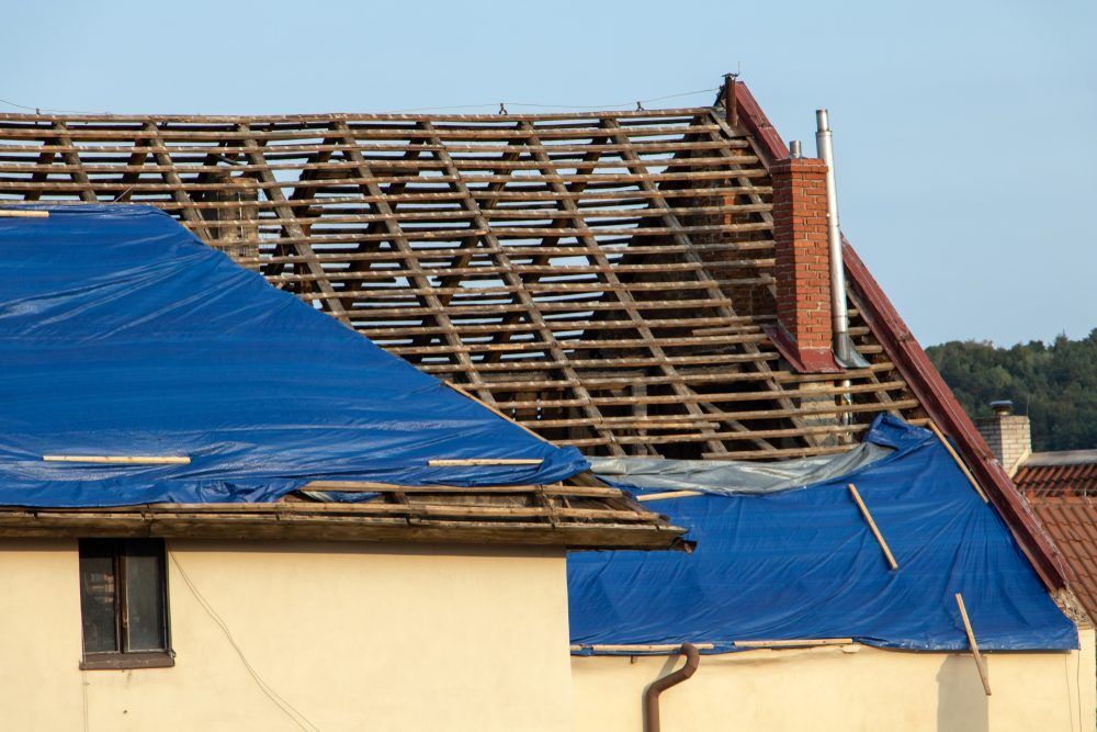 Damaged rooftop with exposed wooden beams and blue tarps — iFix Roofing Geelong In Torquay, VIC