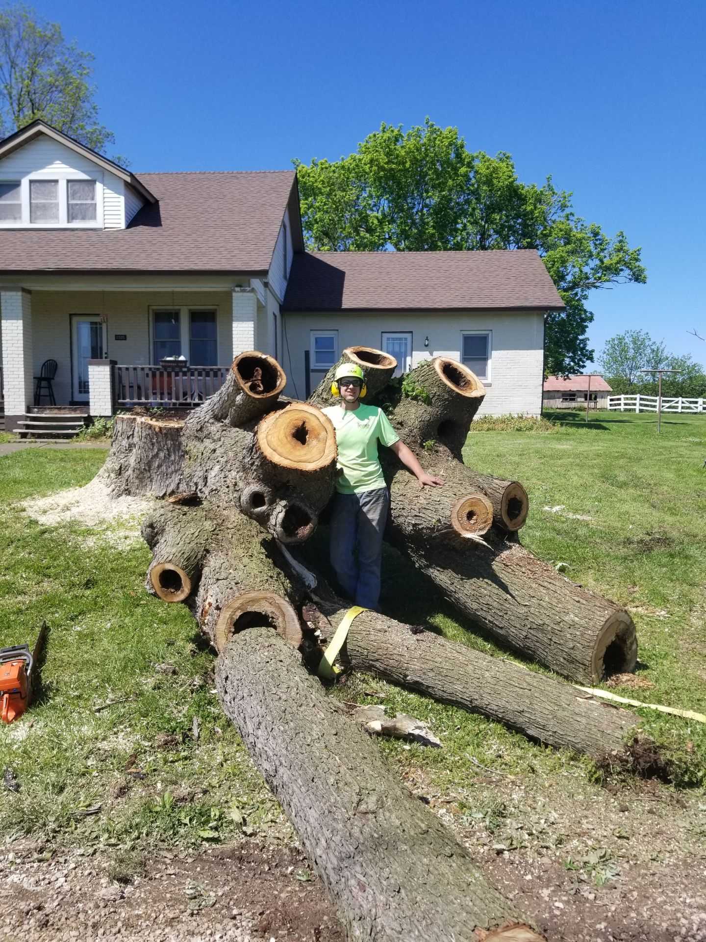 A man is standing next to a pile of logs in front of a house.
