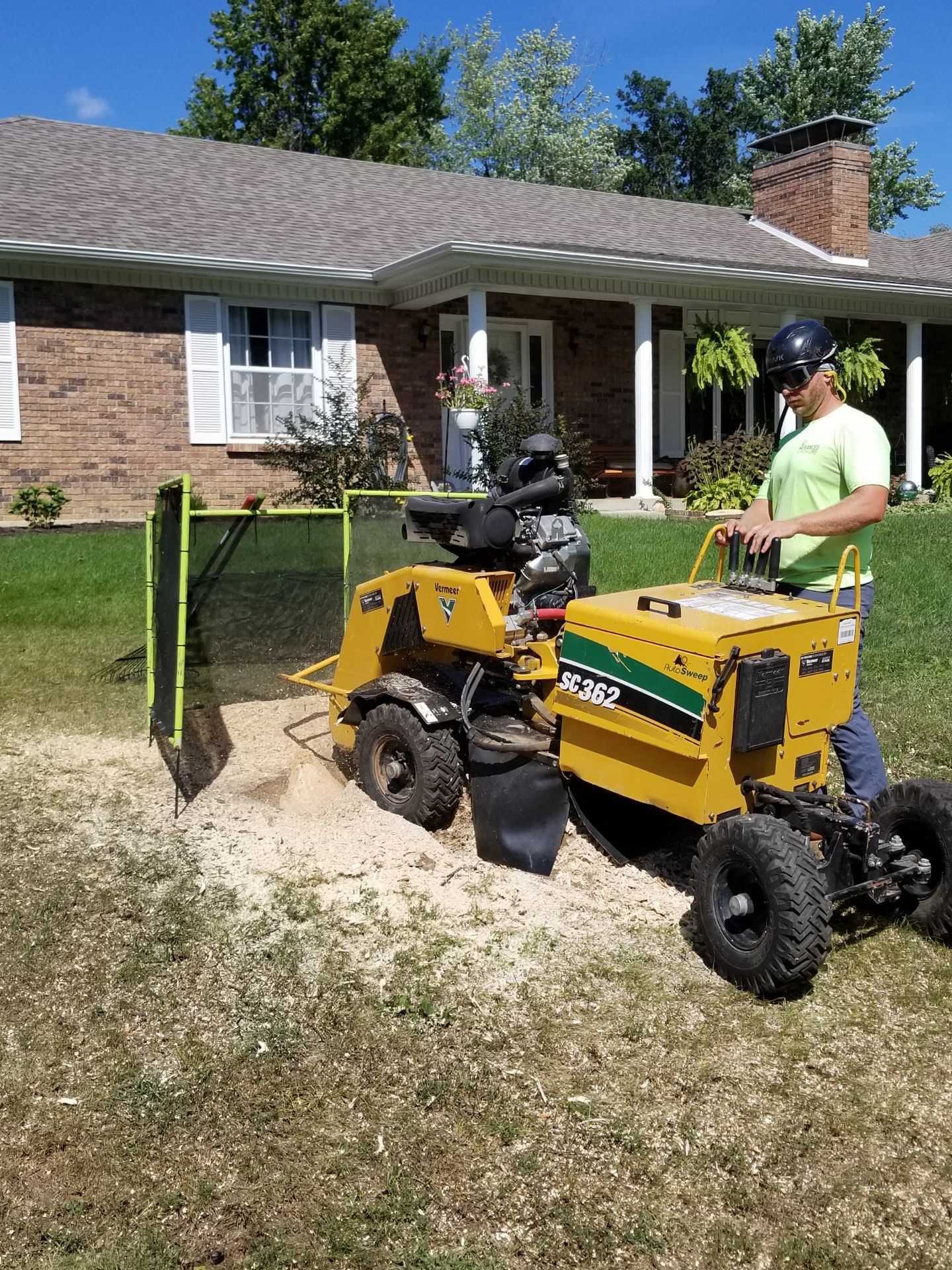 A man is using a stump grinder to remove a tree stump in front of a house.