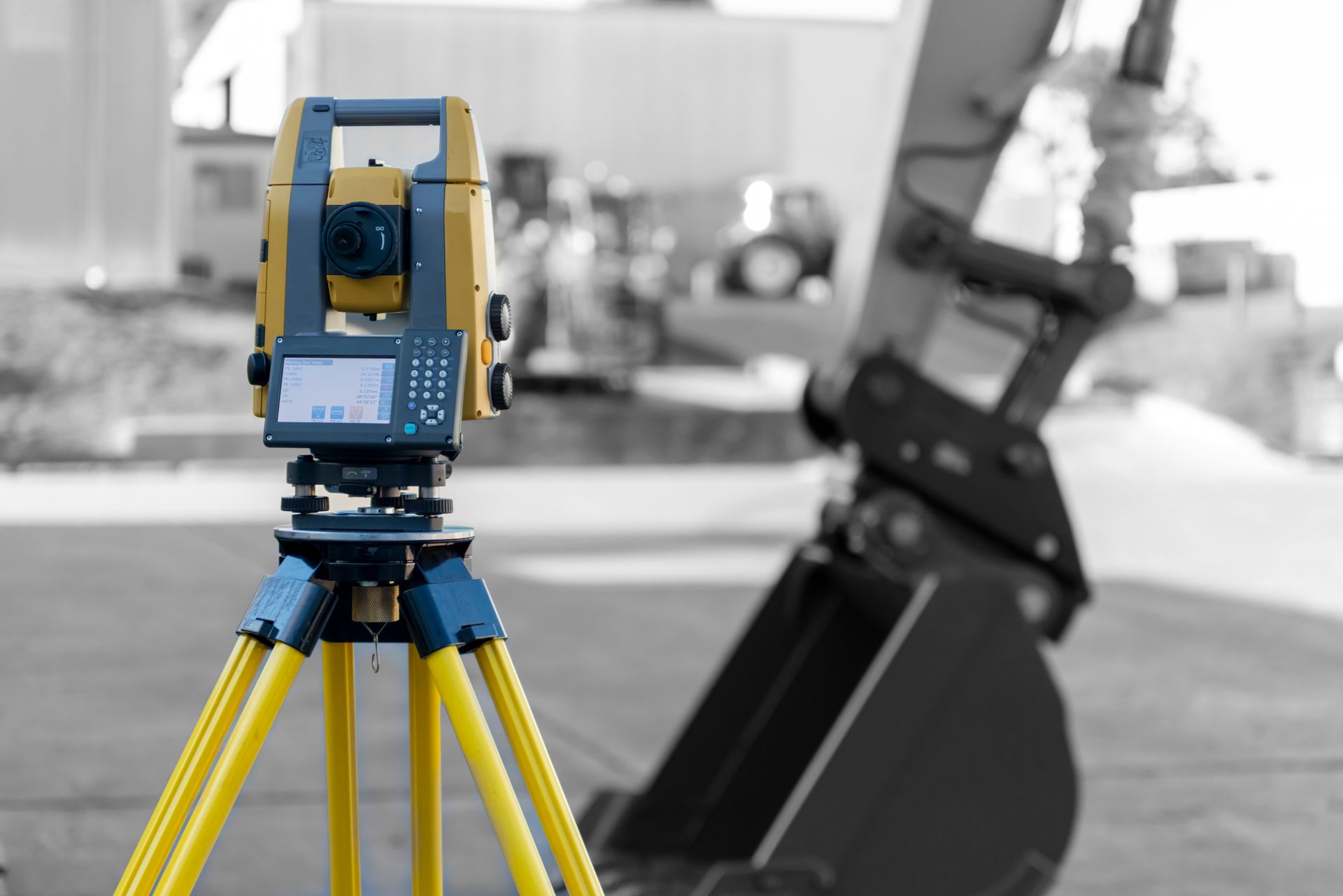 A blue and yellow theodolite is sitting on a tripod in front of a bulldozer bucket.