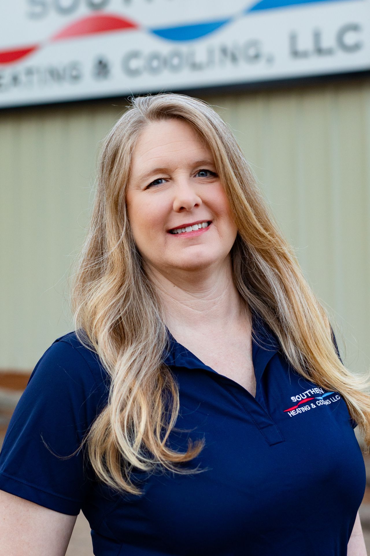 Woman wearing sunglasses in a car, smiling, with long blonde hair, and a blue shirt.