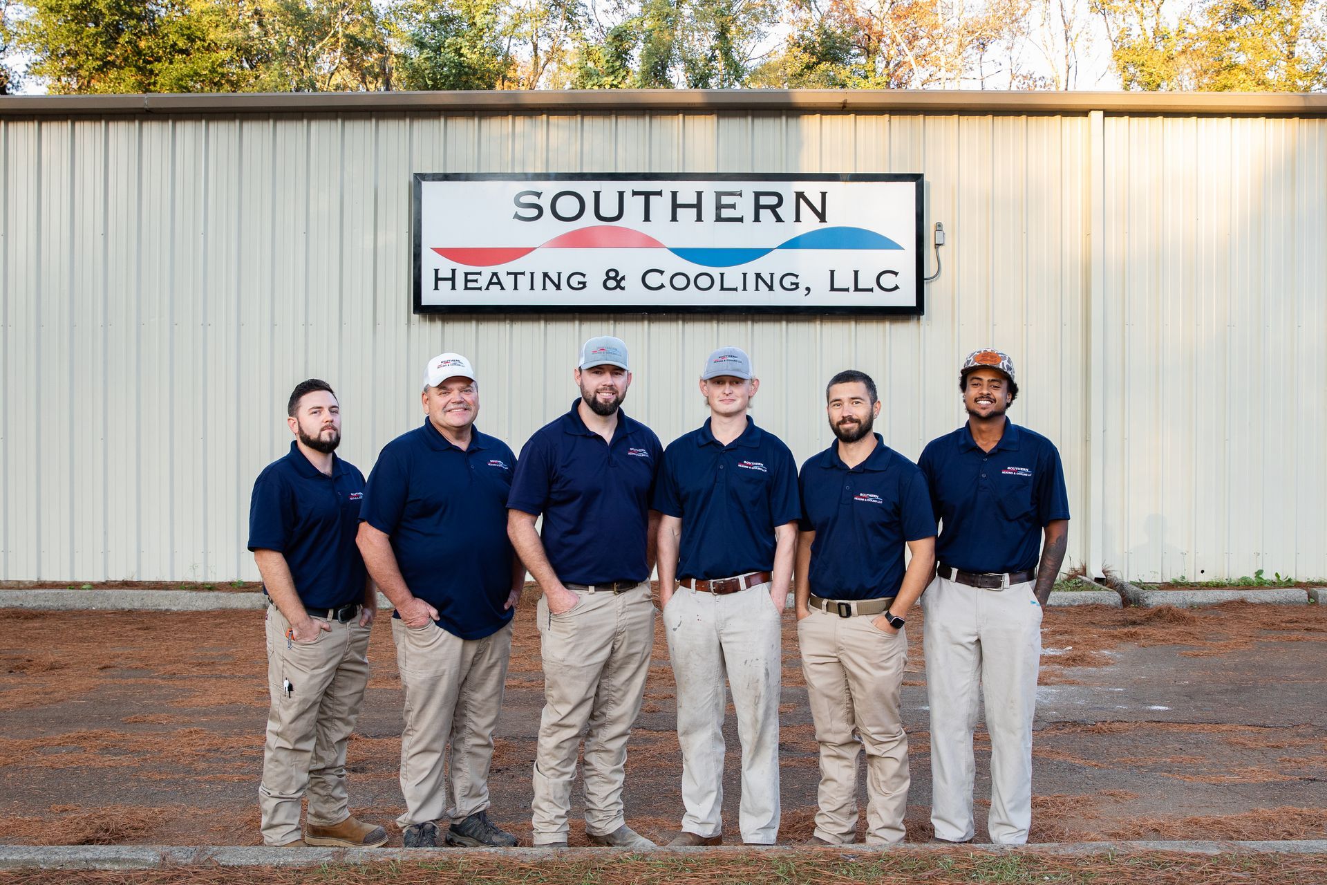 Group of seven employees in work uniforms, standing in front of Southern Heating & Cooling building.