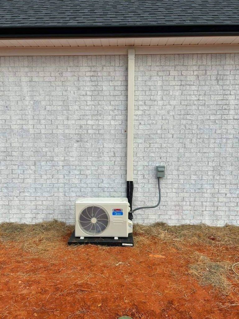 Outdoor air conditioning unit against a painted white brick wall. Electrical conduit and box are visible.