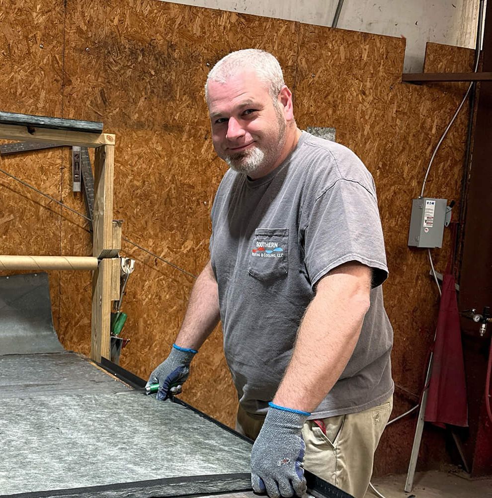 Man wearing gloves smiles while working at a table. Wooden wall backdrop.