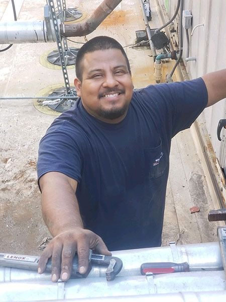 Man in blue shirt, smiling, holding wrench, near pipes.