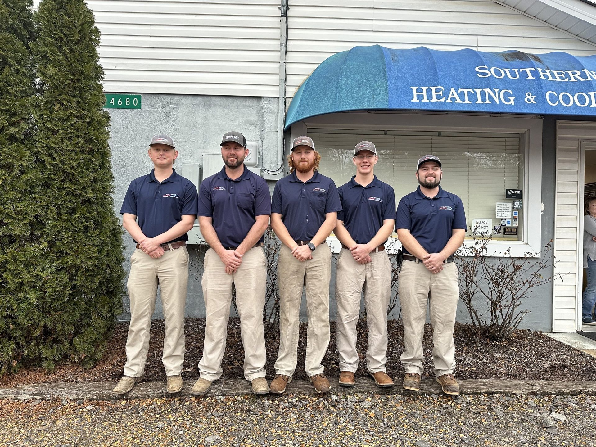 Five men in matching uniforms stand outside a building with 