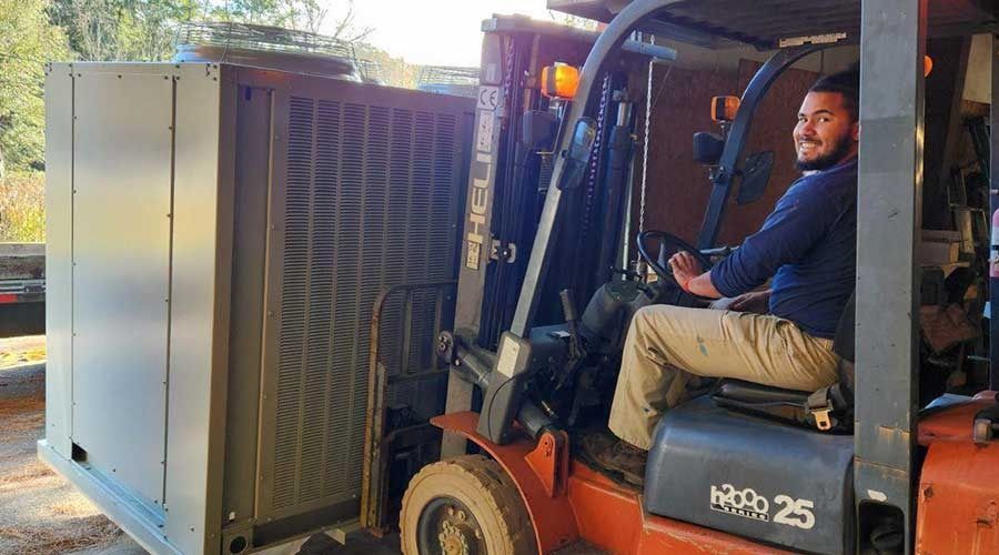 Man operating a forklift, transporting a large, metallic industrial unit outside.