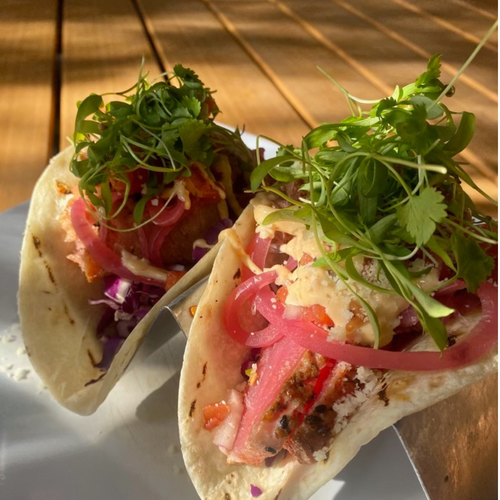 LoonAsea tacos are sitting on a white plate on a wooden table.