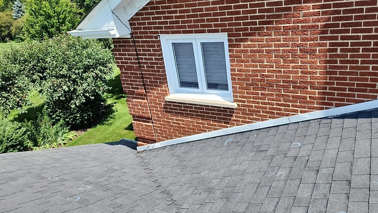 A brick house with a black roof and a white window.