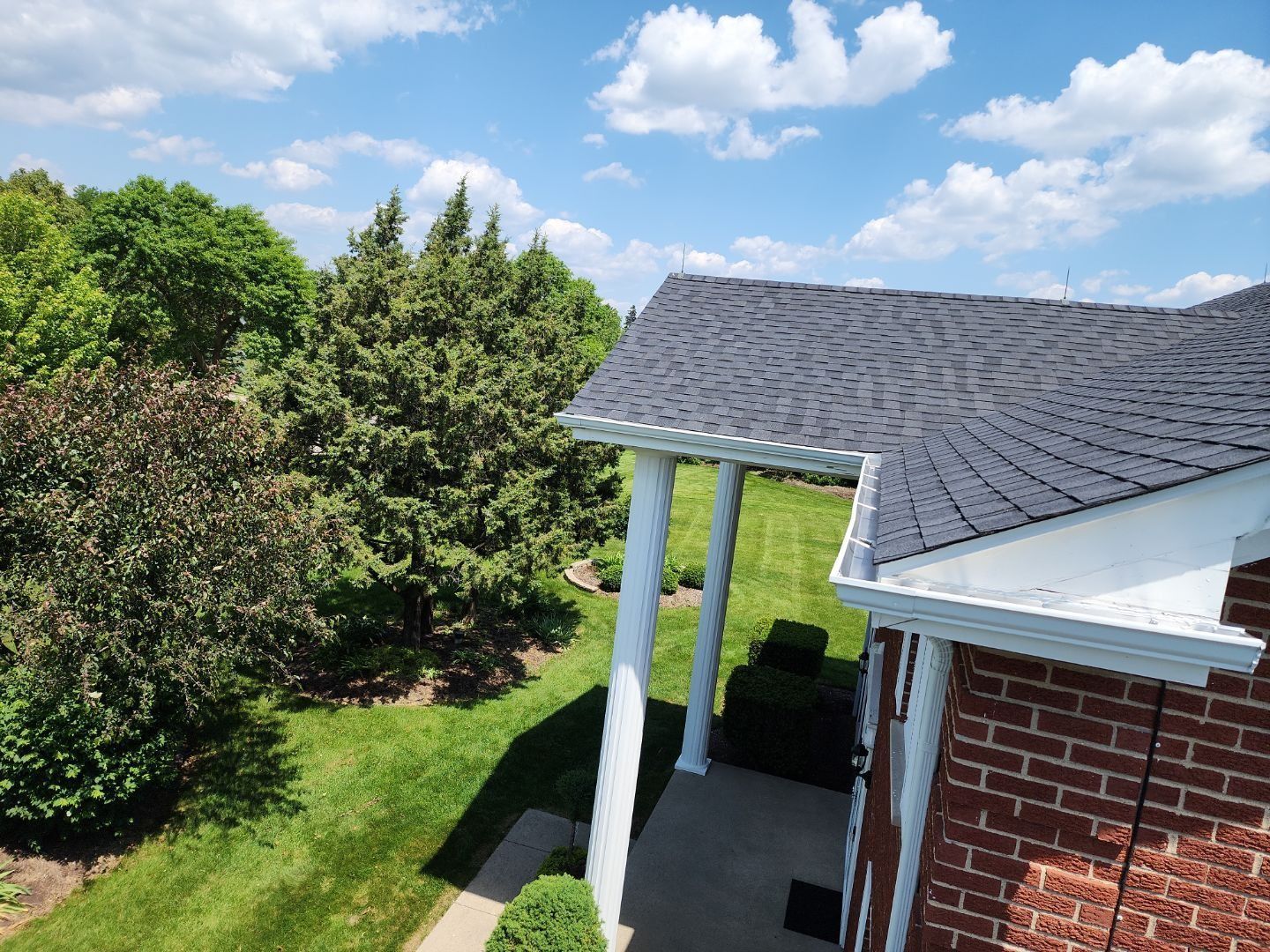An aerial view of a brick house with a porch and trees in the background.