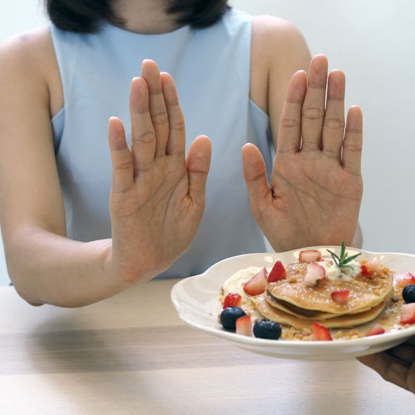 A woman is refusing a plate of pancakes with strawberries and blueberries because of GLP-1 Therapy in NYC by Dr. Dana Cohen, MD