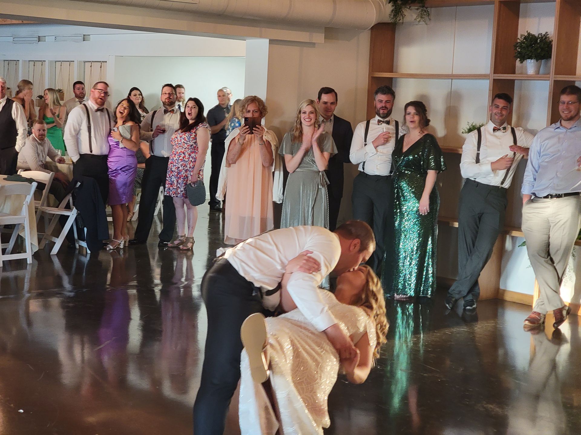 Couple kissing, being dipped on a dance floor, guests watching.