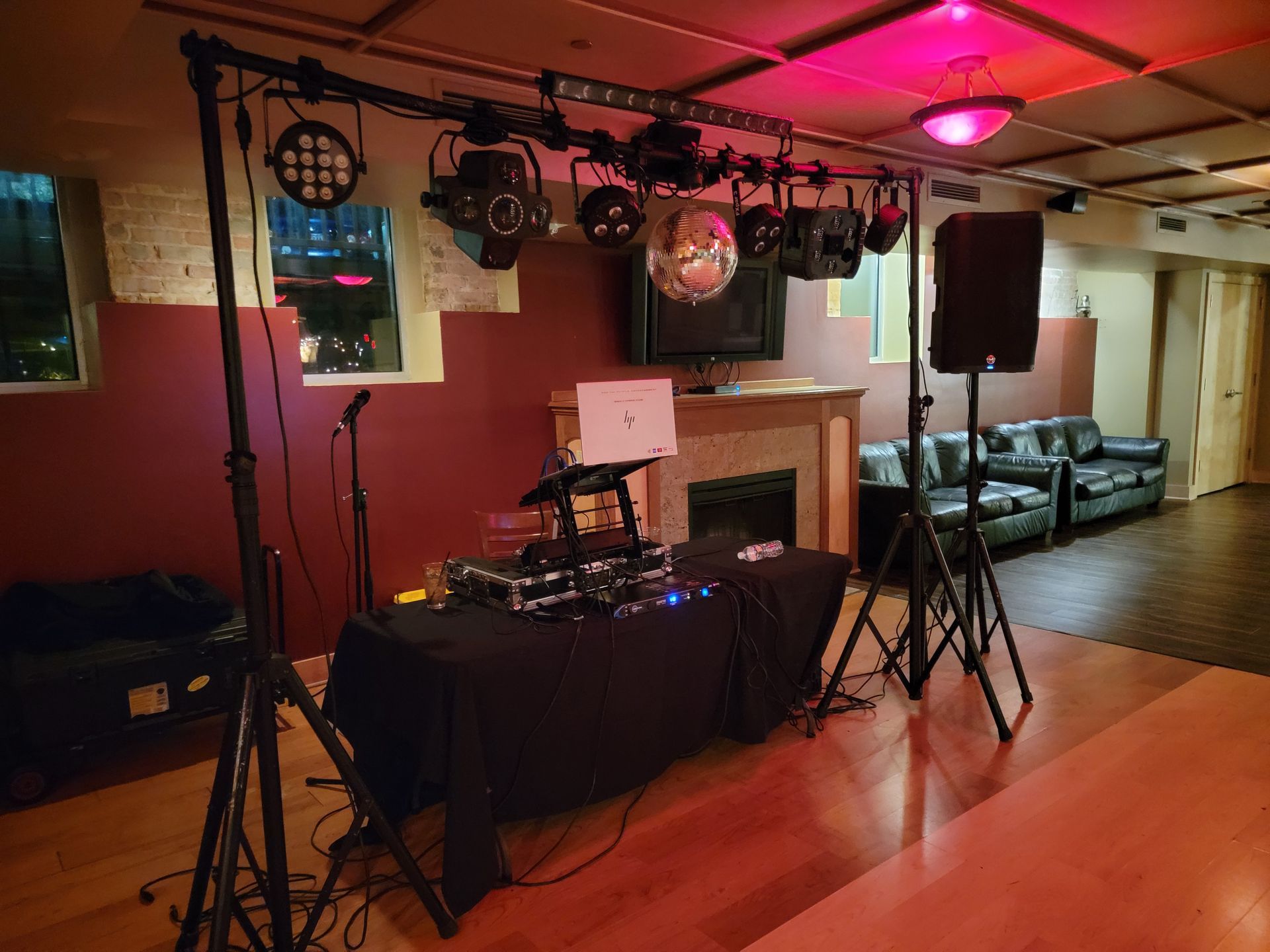 DJ setup in a room with a light rig, disco ball, and speakers. Table with equipment, a laptop.