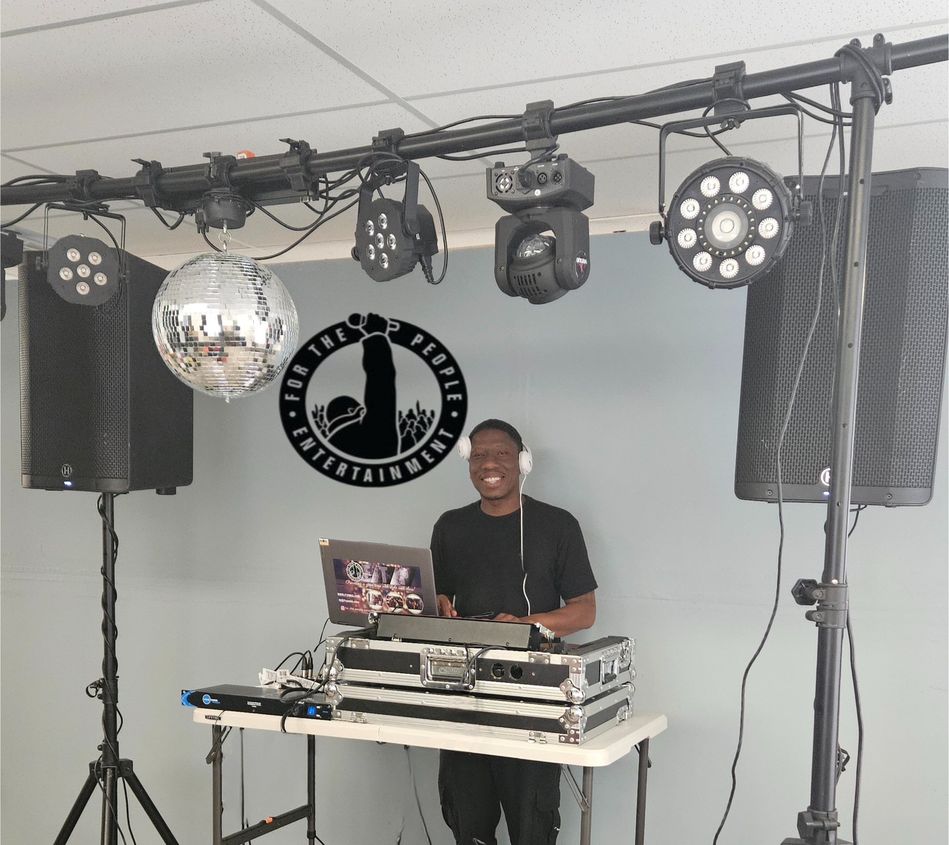 DJ smiling at a party, standing behind a console. Disco ball, lights, and speakers are set up in a room.
