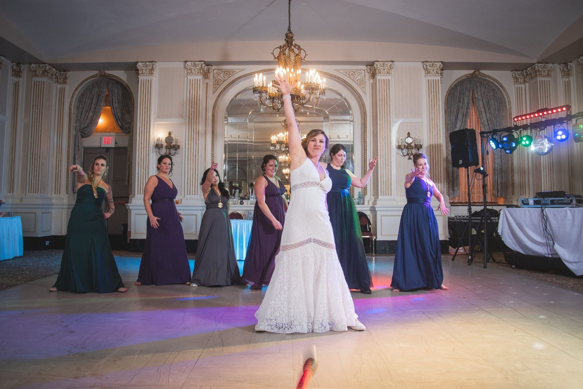 Bride dancing with bridesmaids on a dance floor in an ornate ballroom.