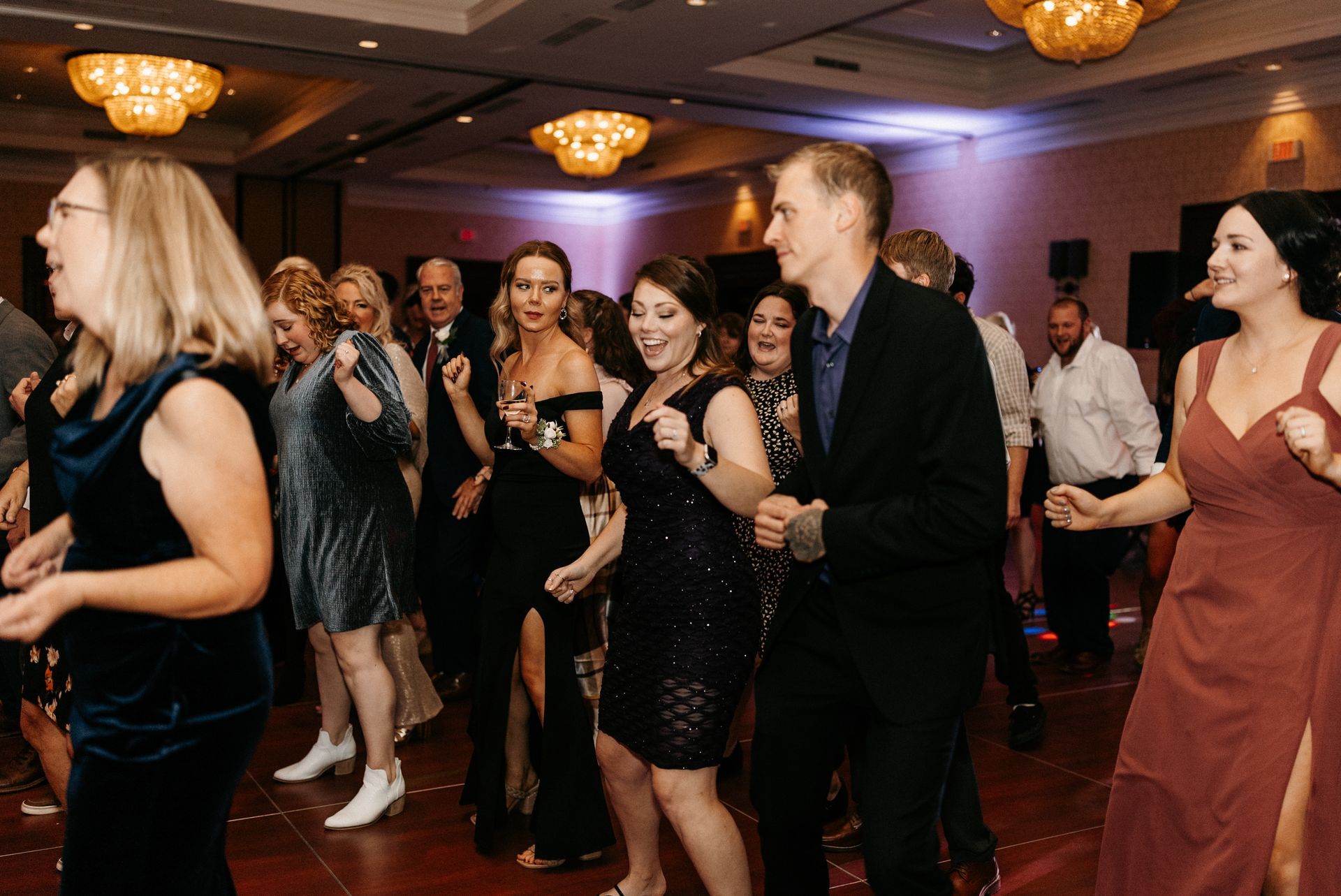 People dancing at a formal event in a ballroom with chandeliers.
