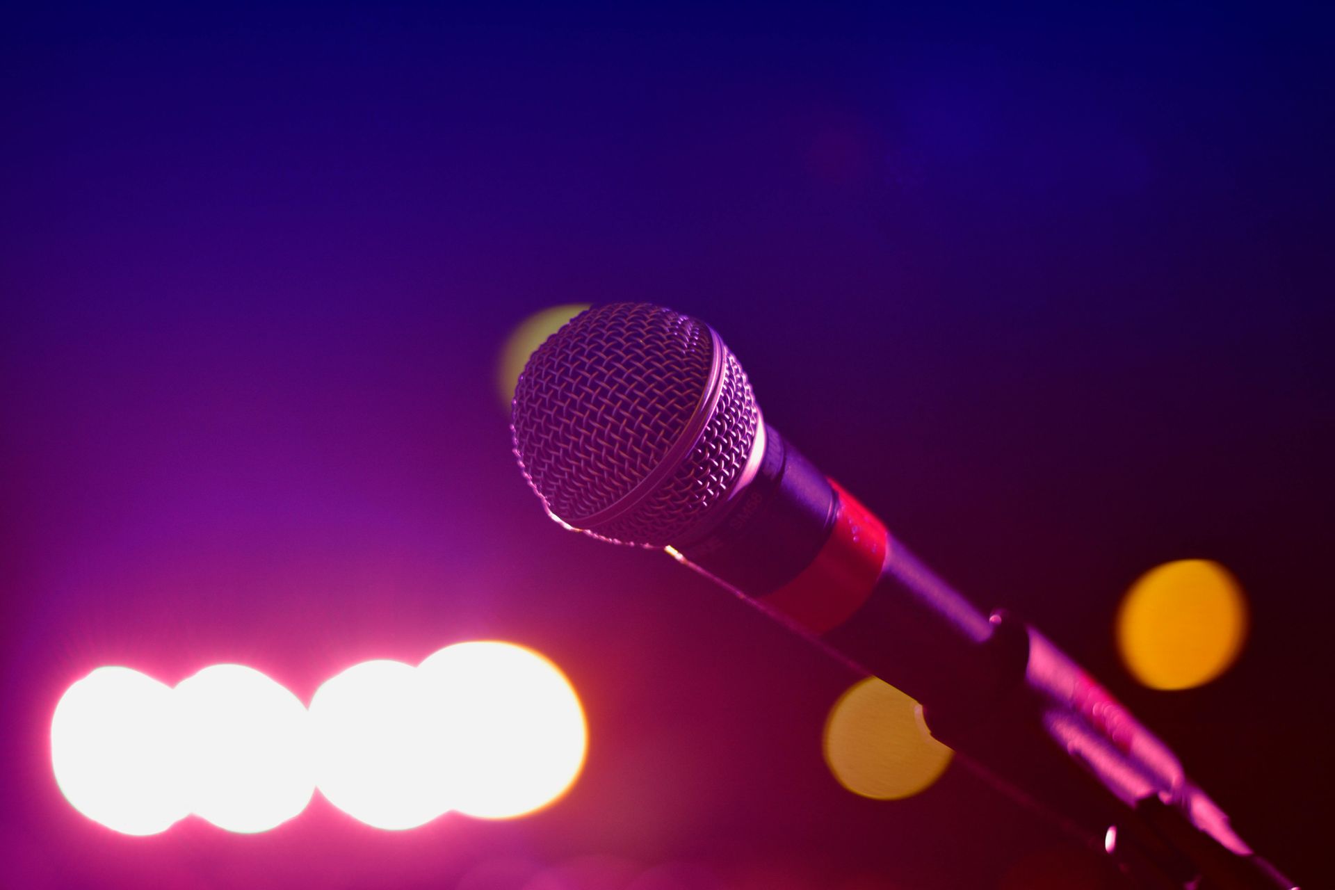 Microphone on stand, purple and pink stage lights in background.