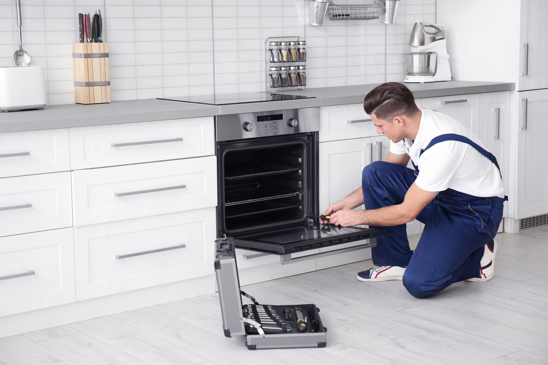 A young man focused on repairing an oven in a well-lit kitchen, using a set of tools to troubleshoot and fix the appliance.