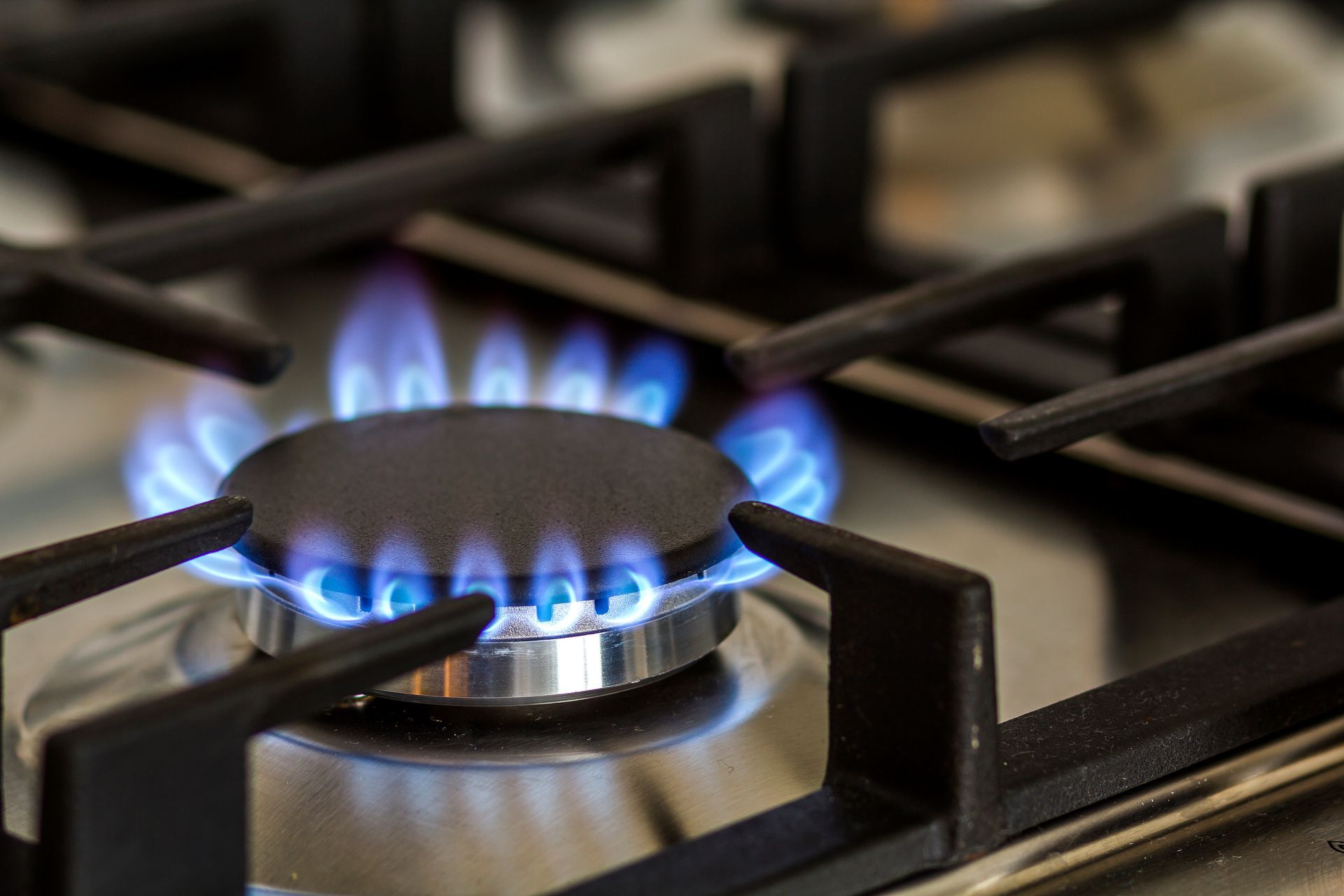 An illuminated gas stove burner in a dimly lit kitchen, with natural gas flames burning brightly.