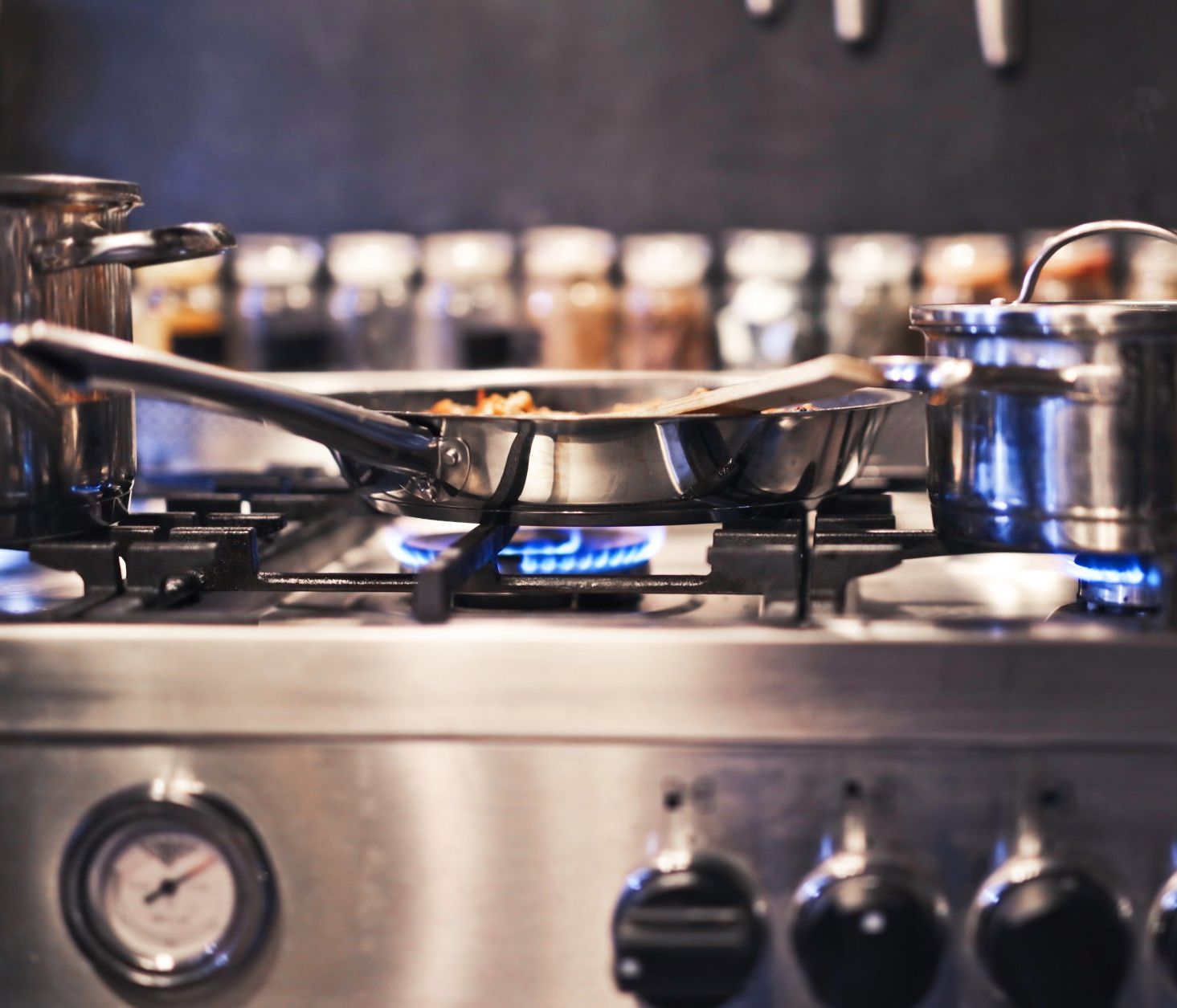 A gas stove with a pan sitting on the burner, emitting flames and heat as it cooks food.