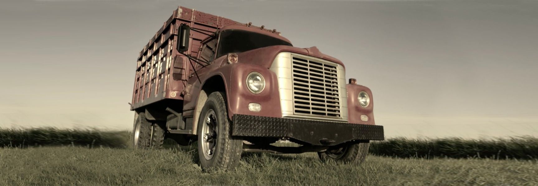 A vintage red farm truck parked on grass, captured from a low-angle perspective under an overcast sky.