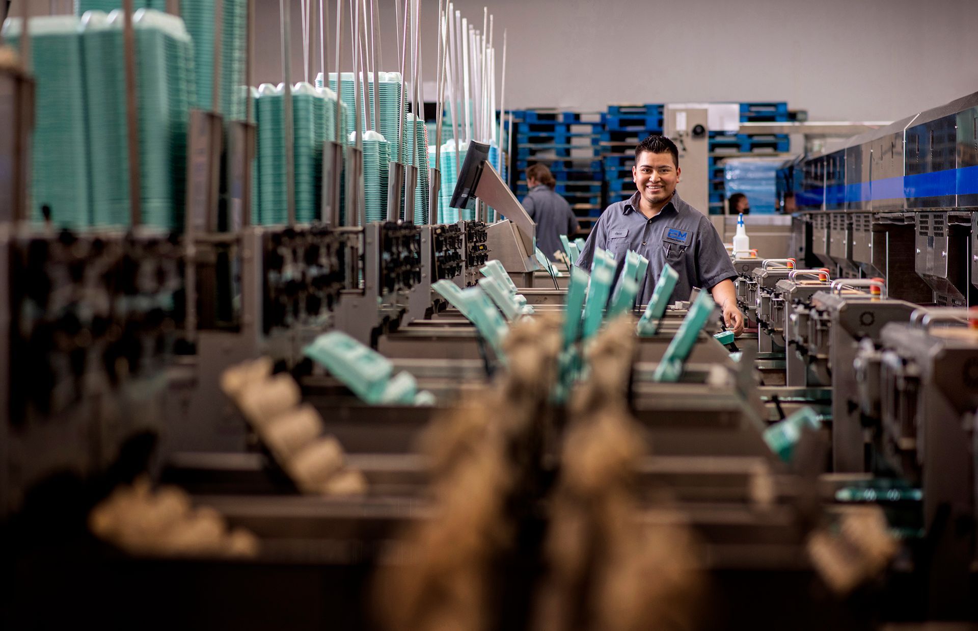 Egg processing line in a factory, with a worker monitoring machines that organize and package eggs.