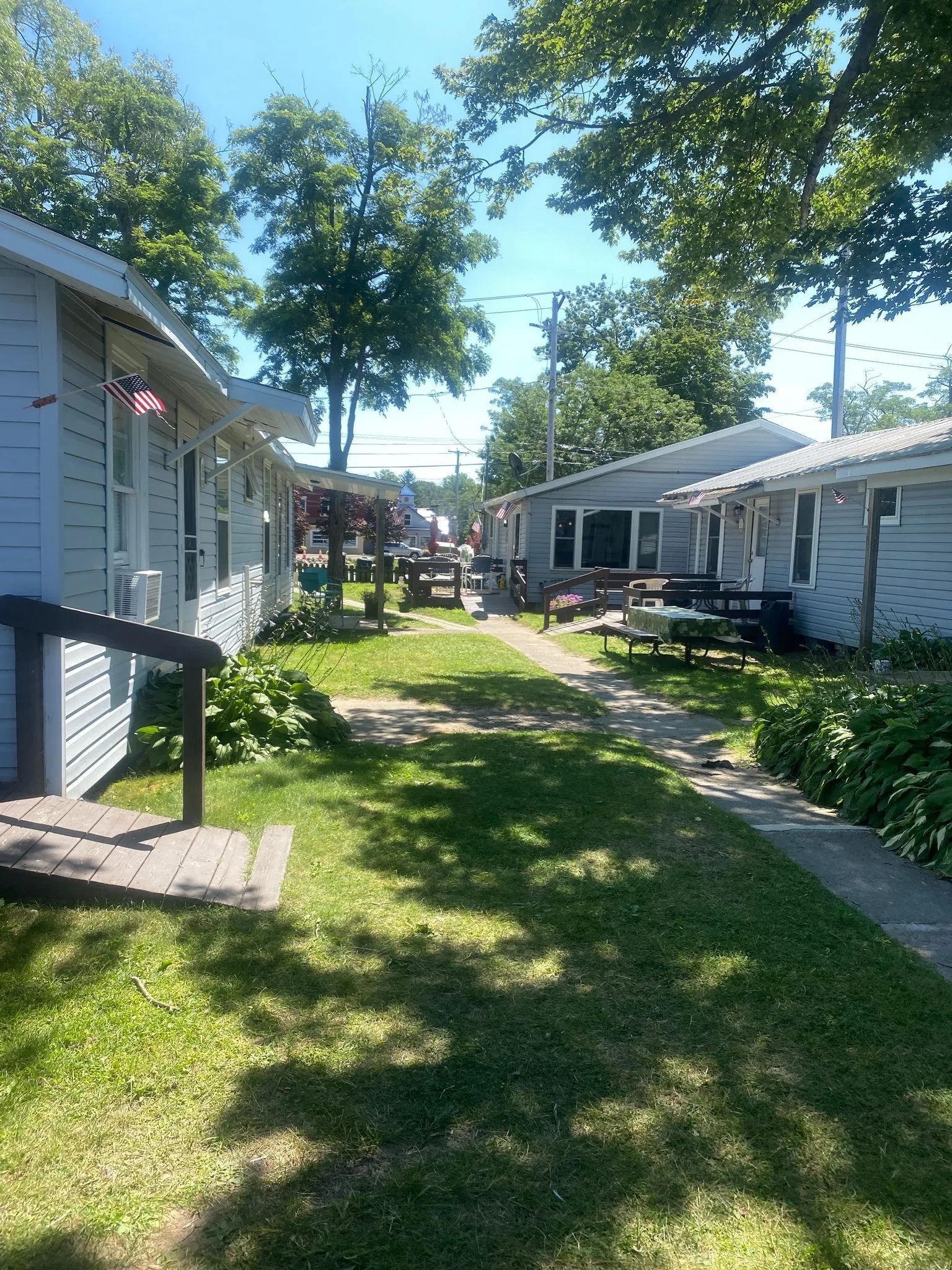 Row of small, light blue cottages with a grassy walkway in between them on a sunny day.