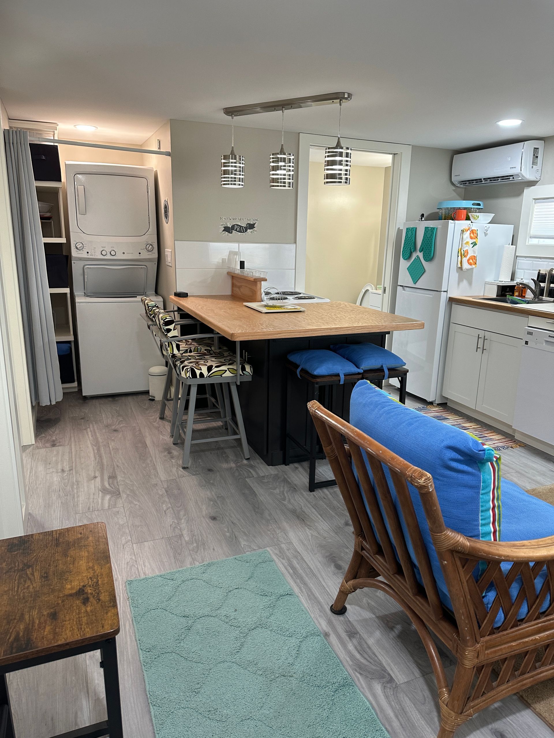 Small kitchen with a stacked washer/dryer, island with stools, and a rattan chair.