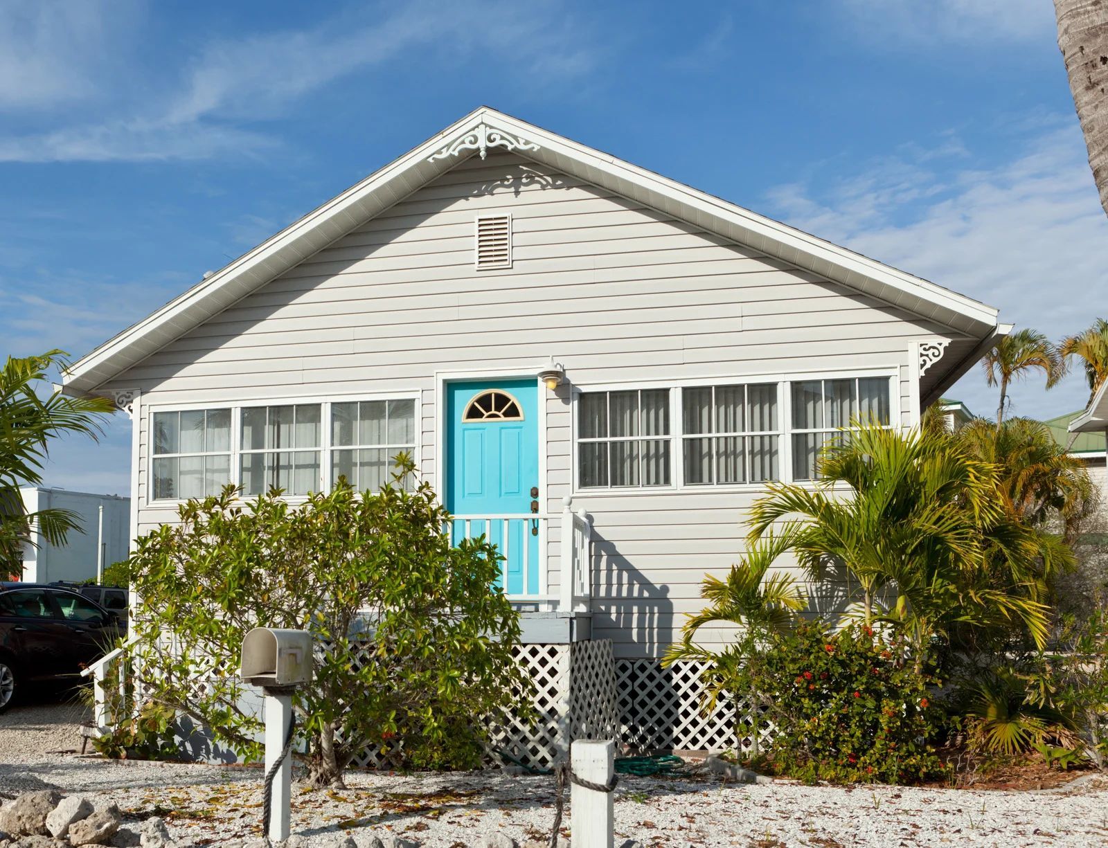 Small white beach house with a turquoise door, windows, and palm trees.