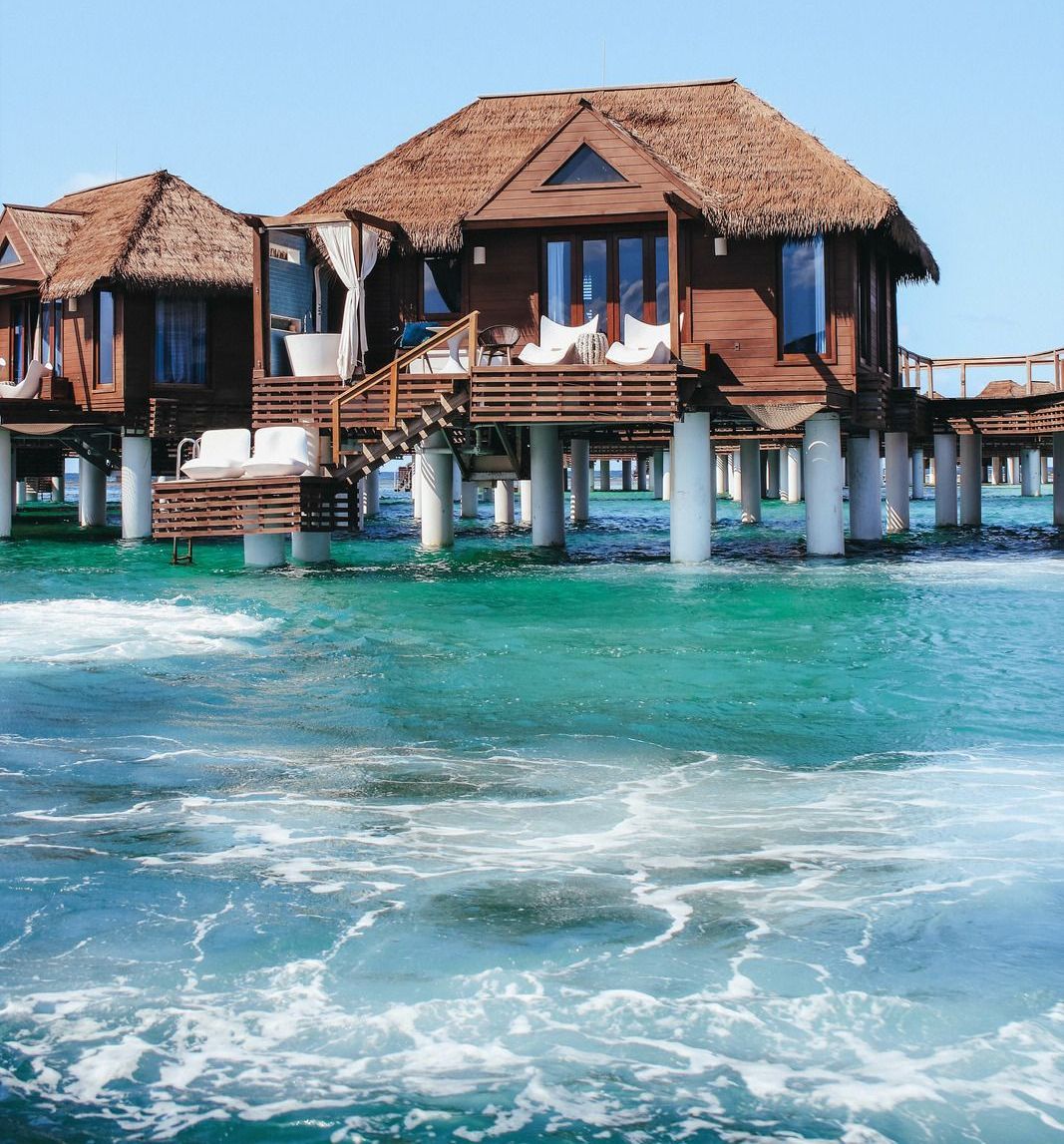 Wooden overwater bungalows with thatched roofs in turquoise water under a clear blue sky.