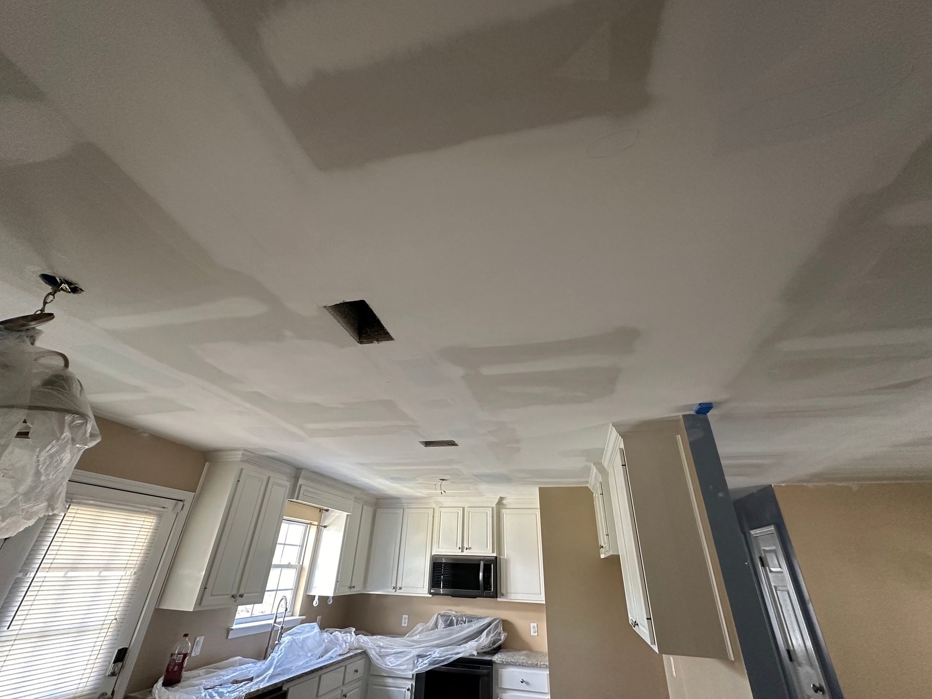 The ceiling of a kitchen is being painted and drywalled.