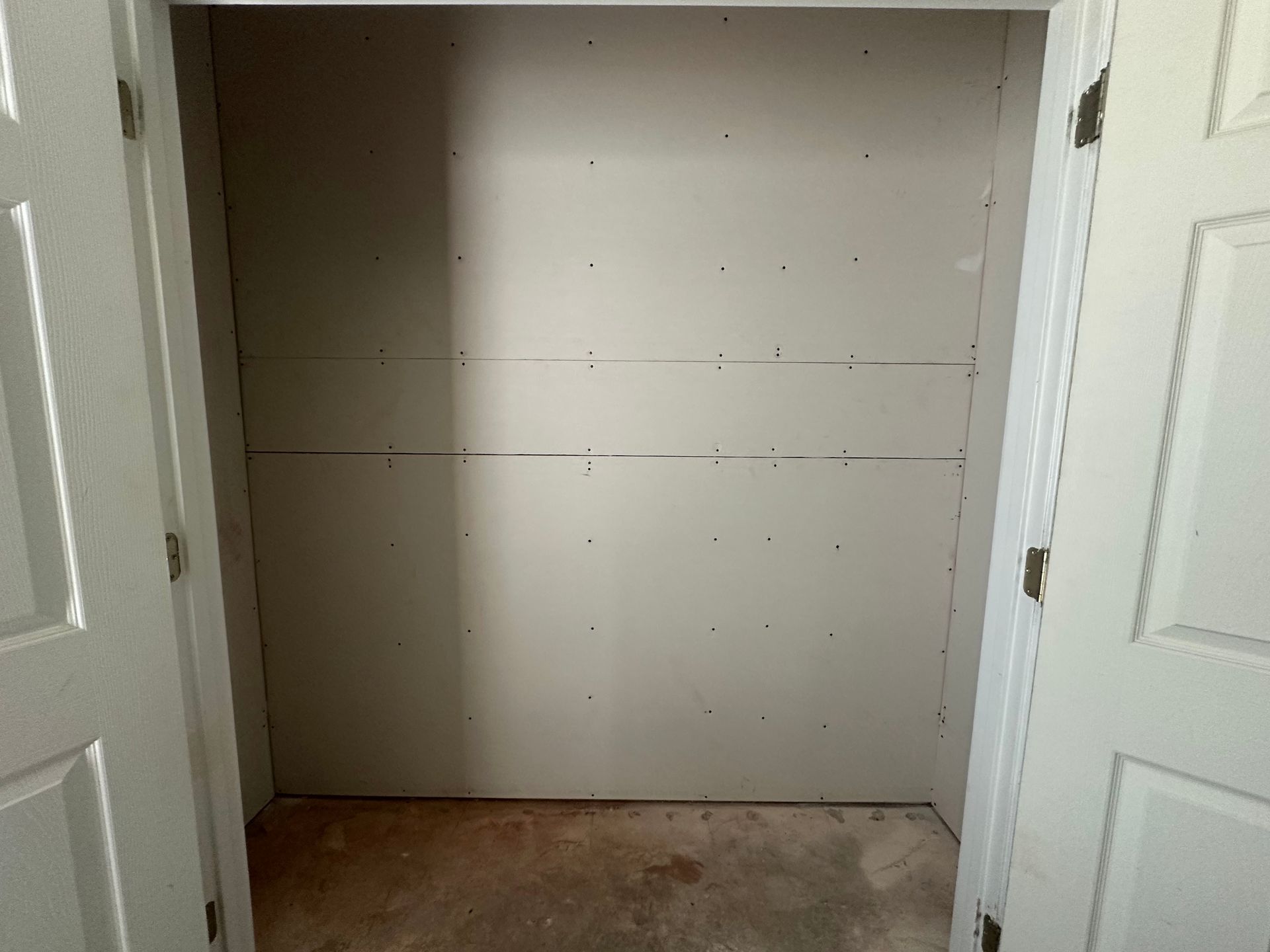 An empty closet with a white door and a white wall.