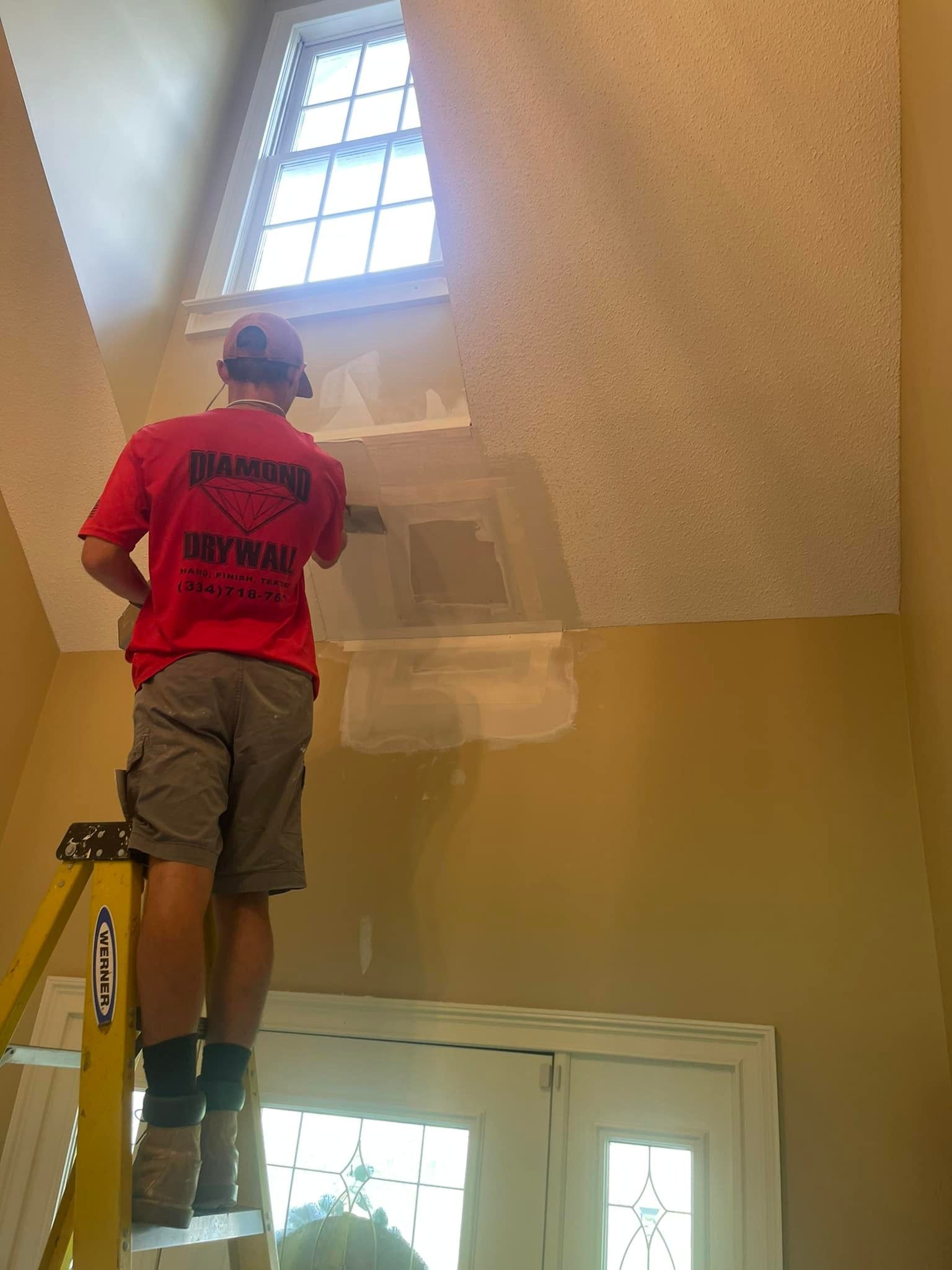 A man in a red shirt is standing on a ladder.