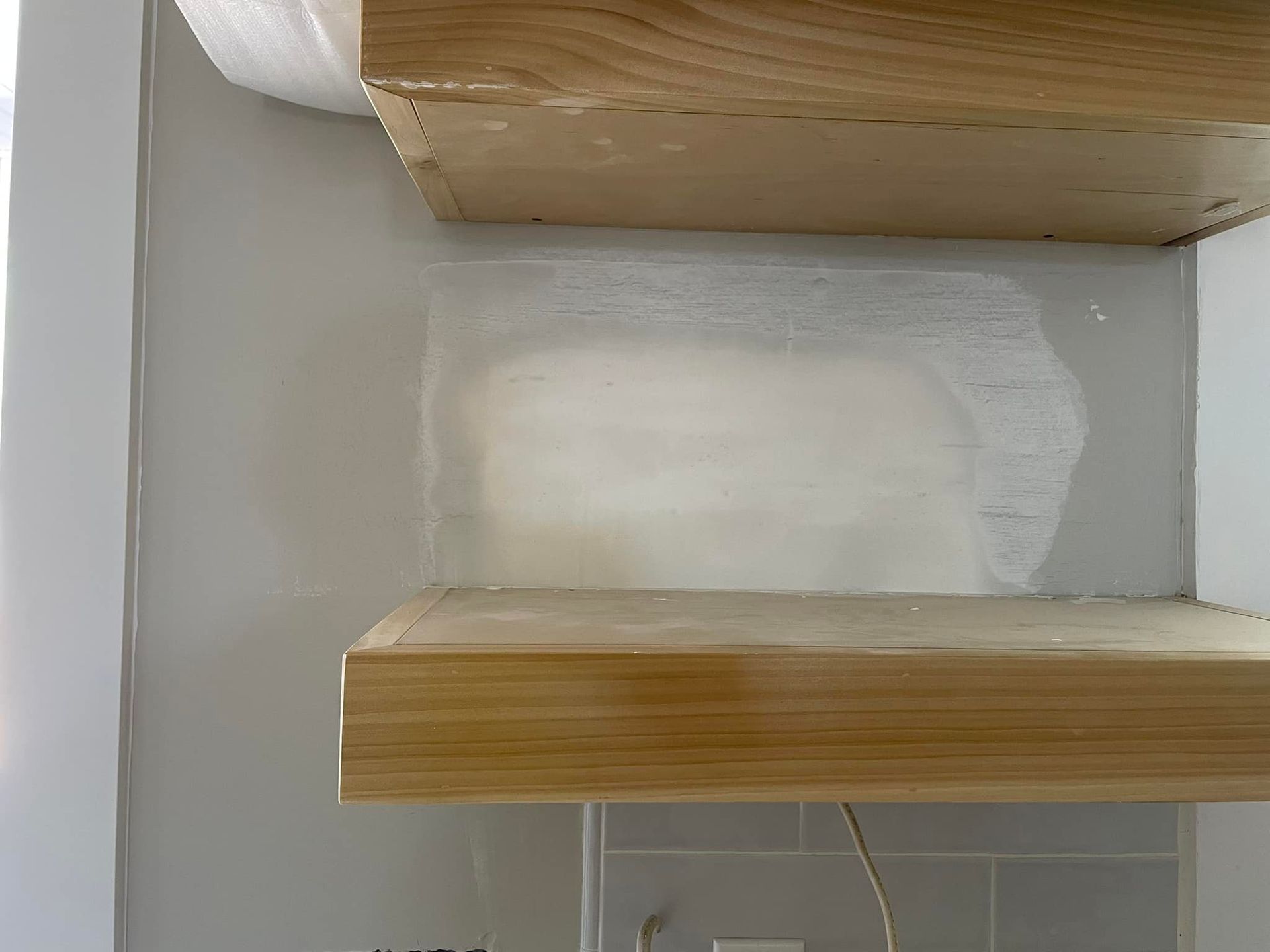A wooden shelf is sitting on top of a white wall.