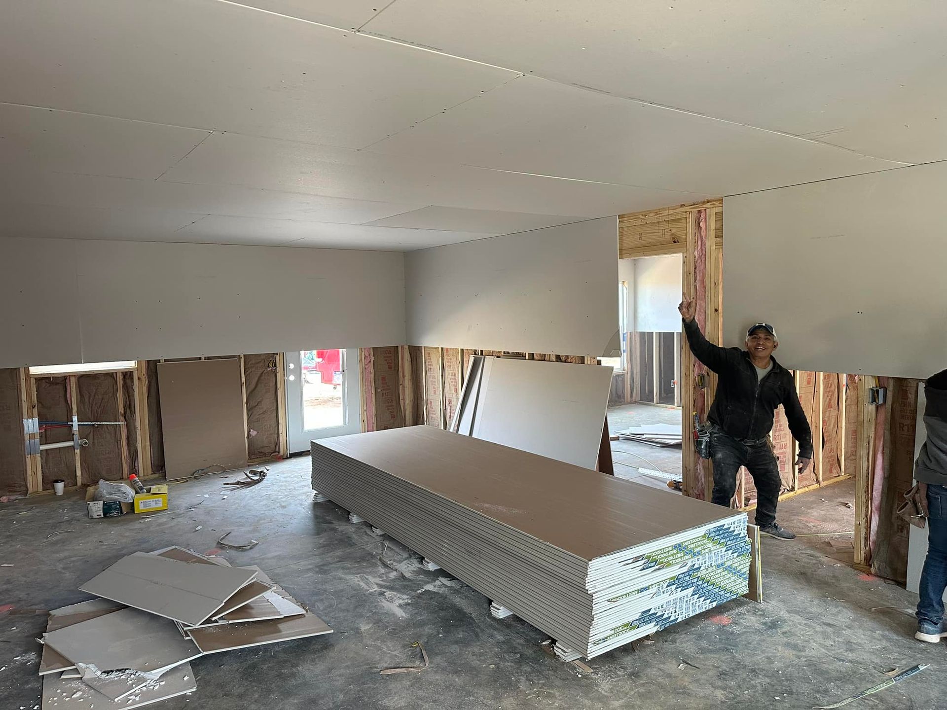 A man is standing in a room with a large stack of drywall.