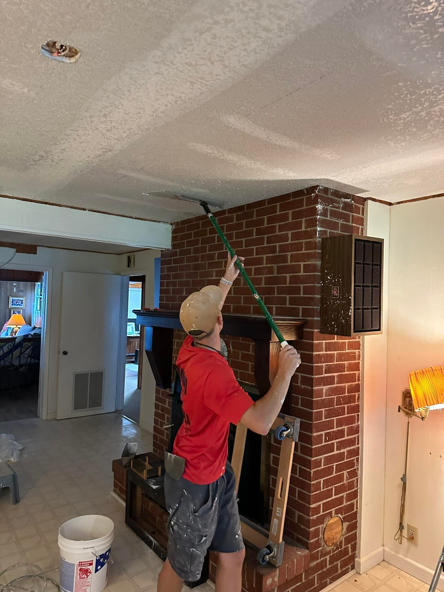 A man is painting the ceiling of a fireplace in a living room.