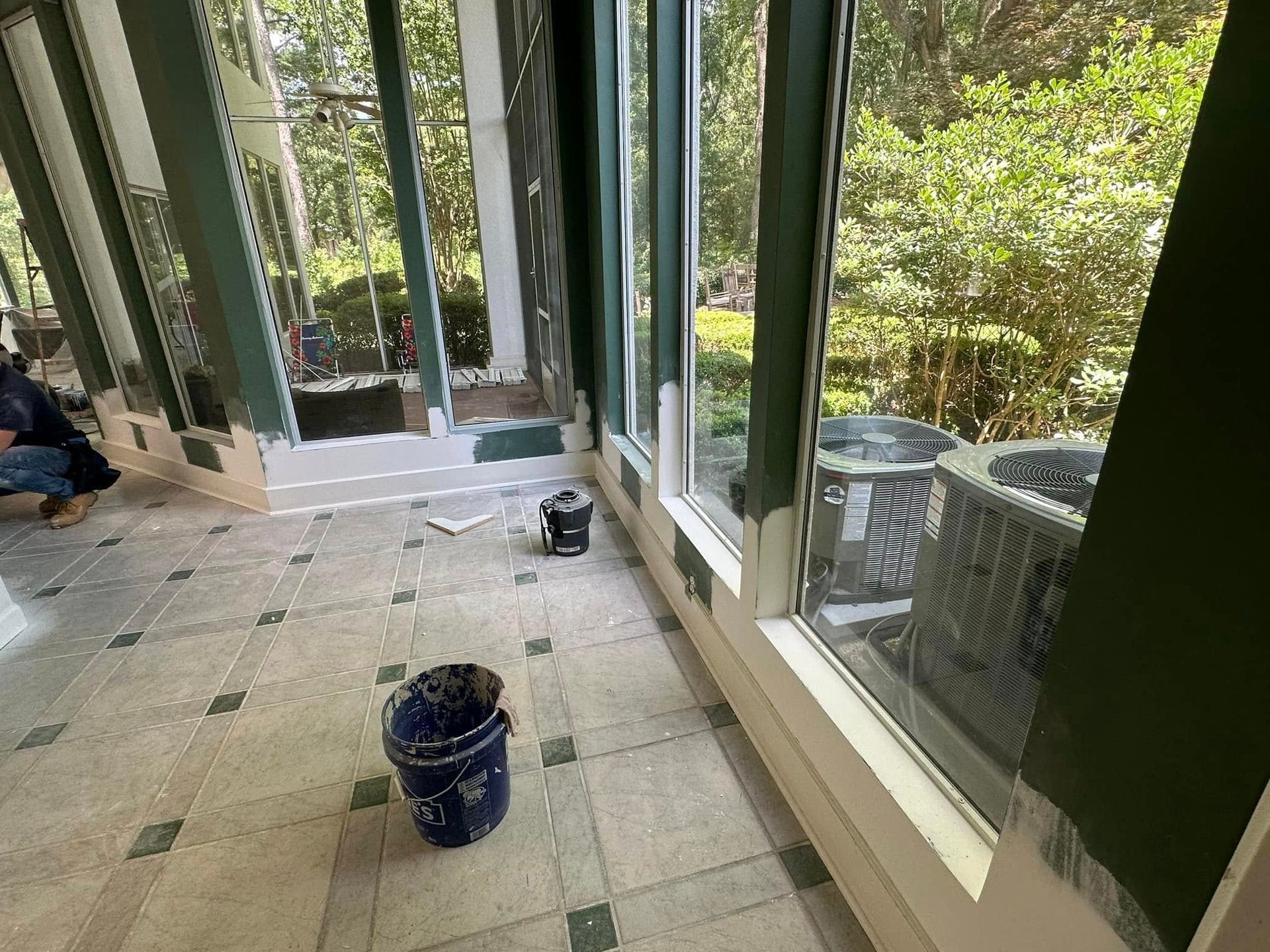 A room with a lot of windows and a bucket of paint on the floor.