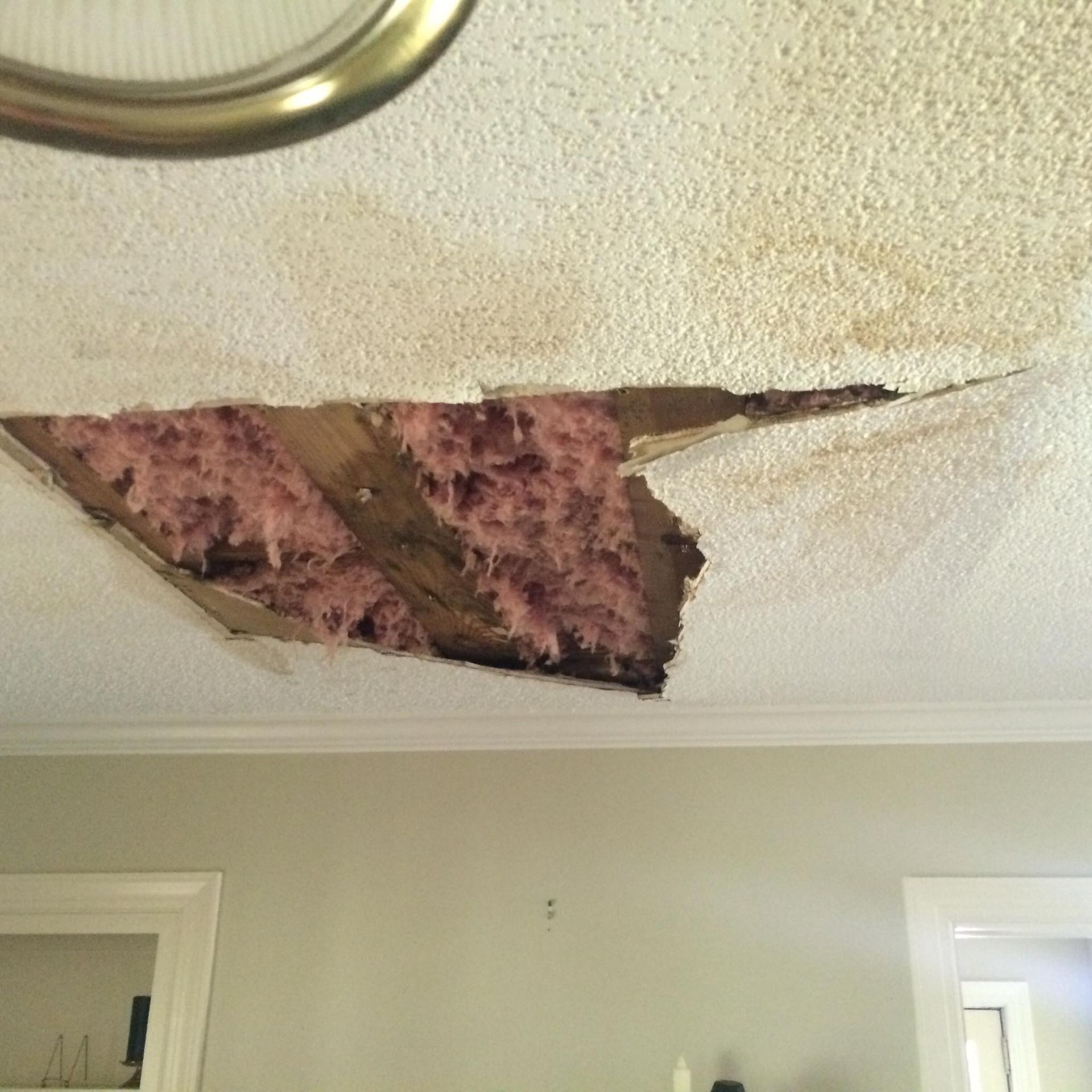 A room with a hole in the ceiling that has pink insulation coming out of it