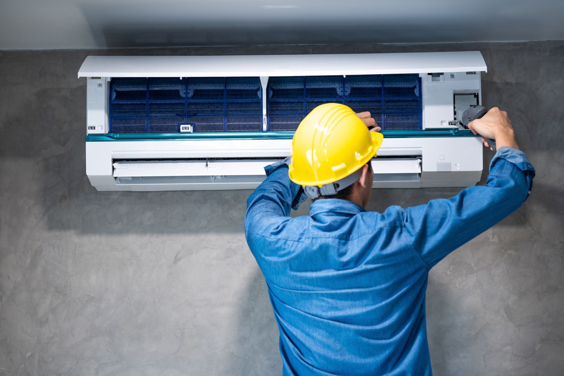 A technician installing a wall-mounted air conditioner with a screwdriver in a bedroom. A technician installing a wall-mounted air conditioner with a screwdriver in a bedroom.