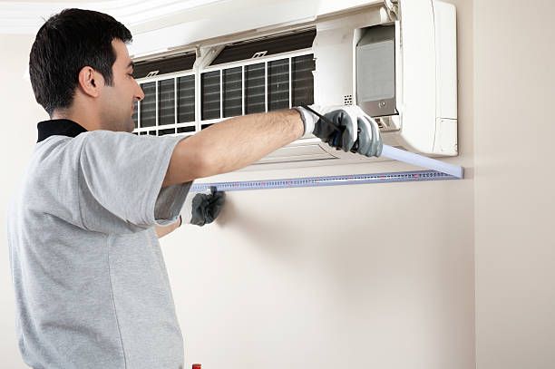 A technician wearing gloves is taking wall measurements for AC installation in a residential room.