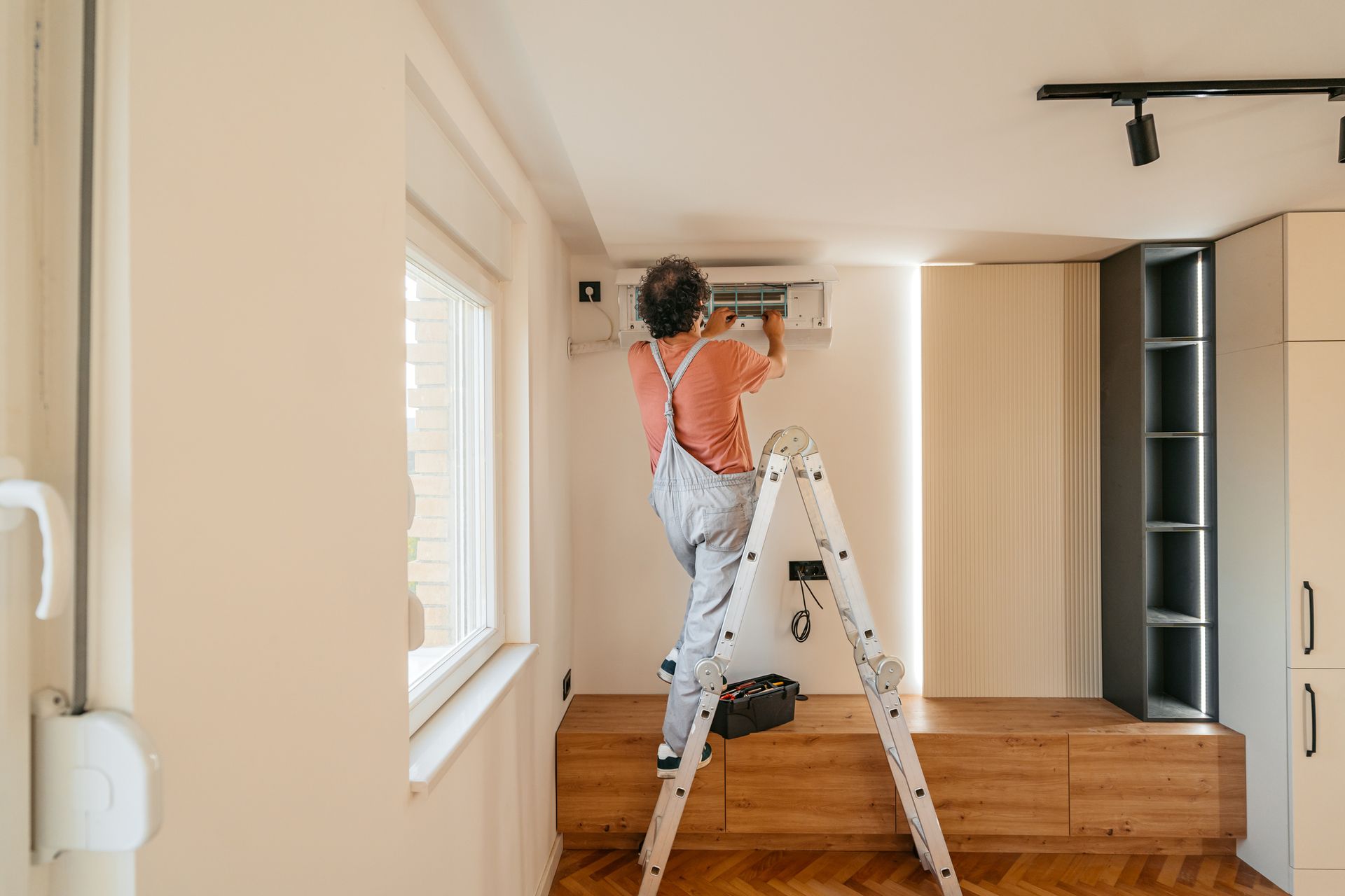 An electrician in overalls is fixing the AC of a house.