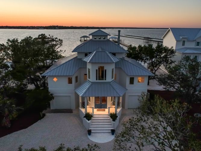 An aerial view of a white house with a gray roof overlooking a body of water